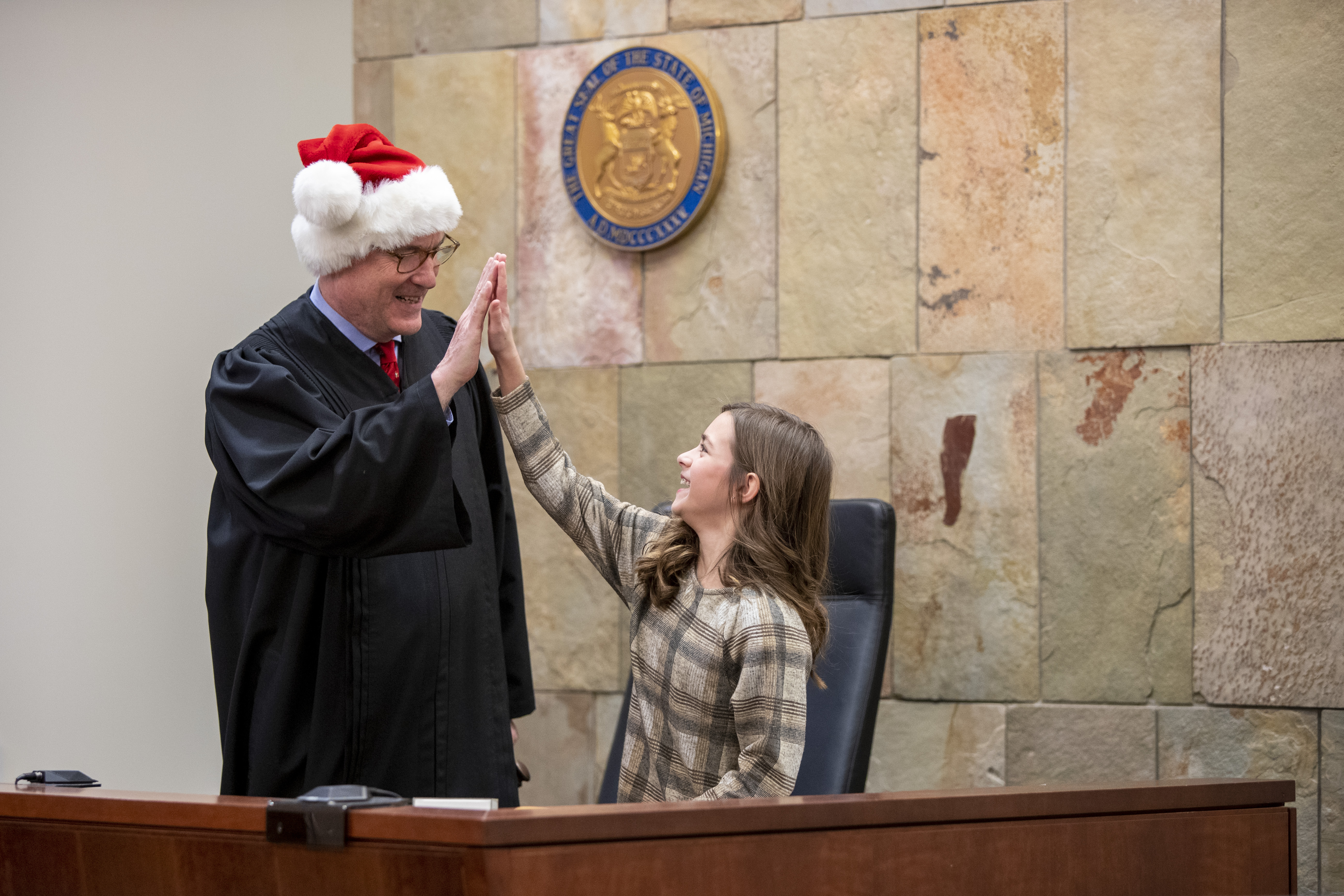 Judge T.J. Ackert gives a high five to Corryn Myers, 10, after letting her use his gavel during Adoption Day at the Kent County Courthouse in Grand Rapids on Thursday, Dec. 8, 2022. Corryn’s parents, Tammy and Jordan Myers, are the biological parents of 1-year-old twins Eames and Ellison. Lauren Vermilye, a surrogate, gave birth to the twins after Tammy went through breast cancer treatment and has no claim to the babies. The Myers family was able to adopt the twins after convincing the court system to grant them custody. (Cory Morse | MLive.com)