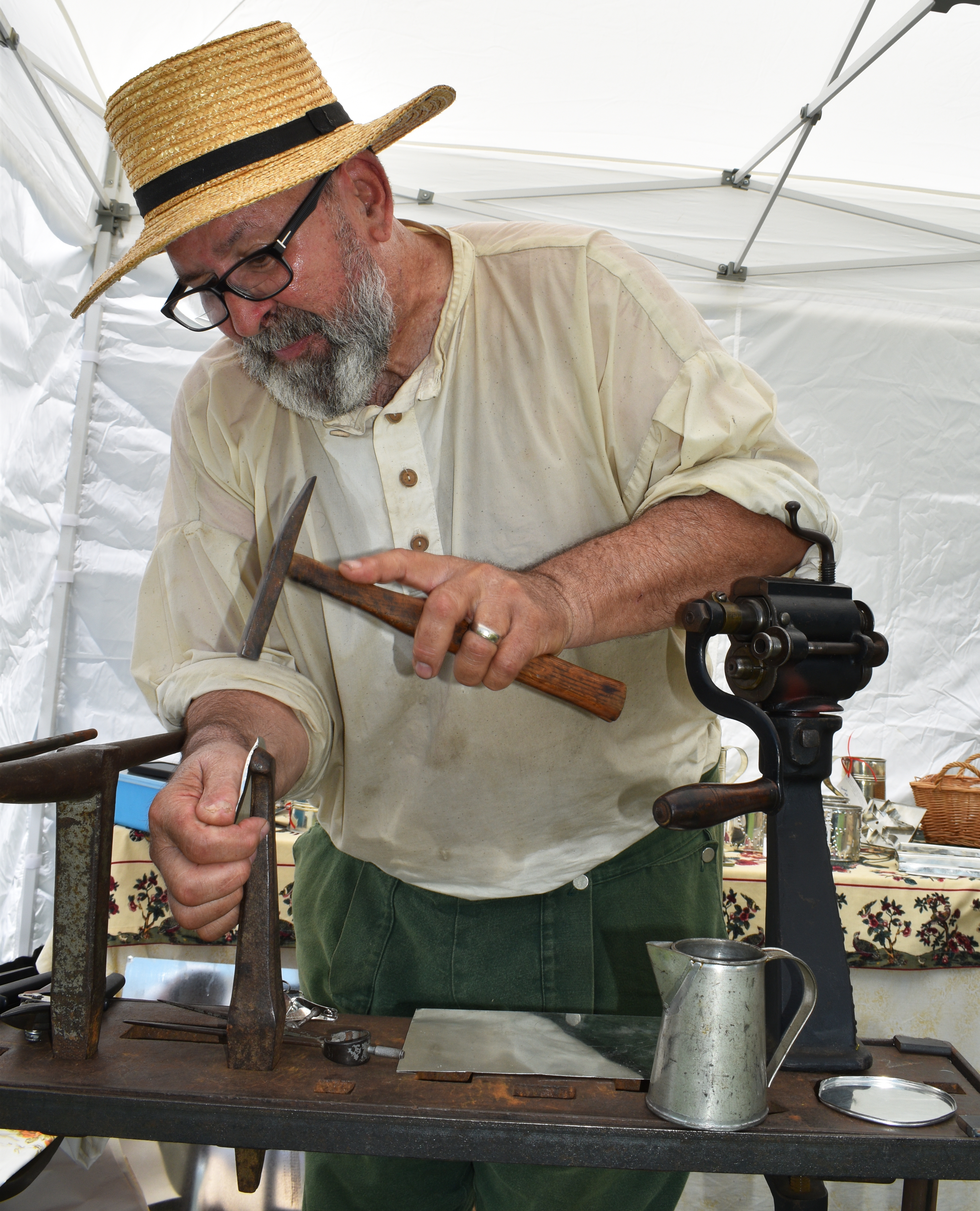 Ken Smith, from Ken Smith’s Backyard Tin Shop in Kutztown, demonstrates shaping tin with the stake-and-hammer method from pre-1820 beside an 1840s-era hand-cranked machine that made the job more efficient, as Historic Bethlehem Museums & Sites opens its two-day Blueberry Festival & Market To Go on Saturday, July 13, 2024, that continues Sunday at Burnside Plantation.