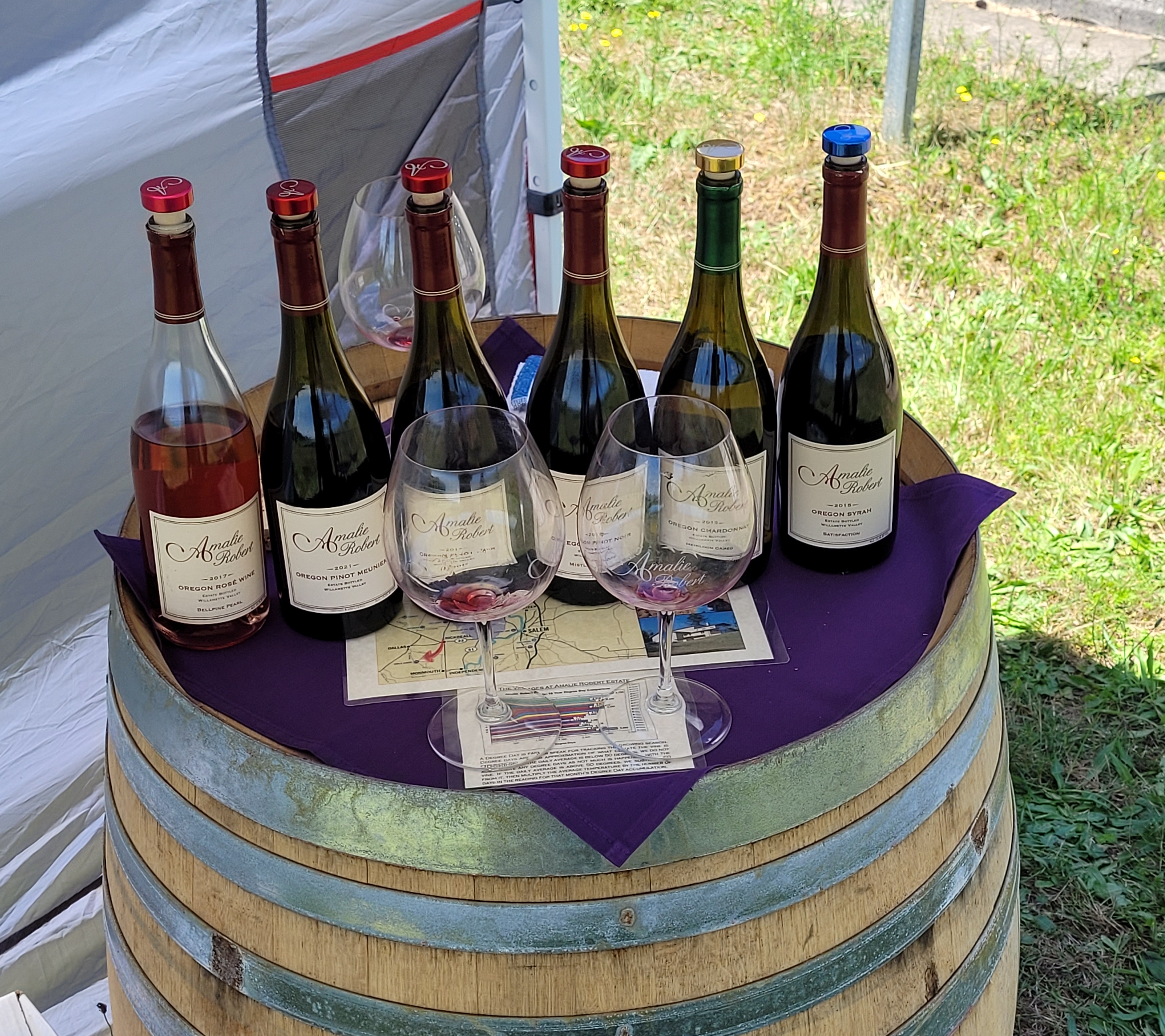A wine barrel holds a half-dozen wine. bottles on top.