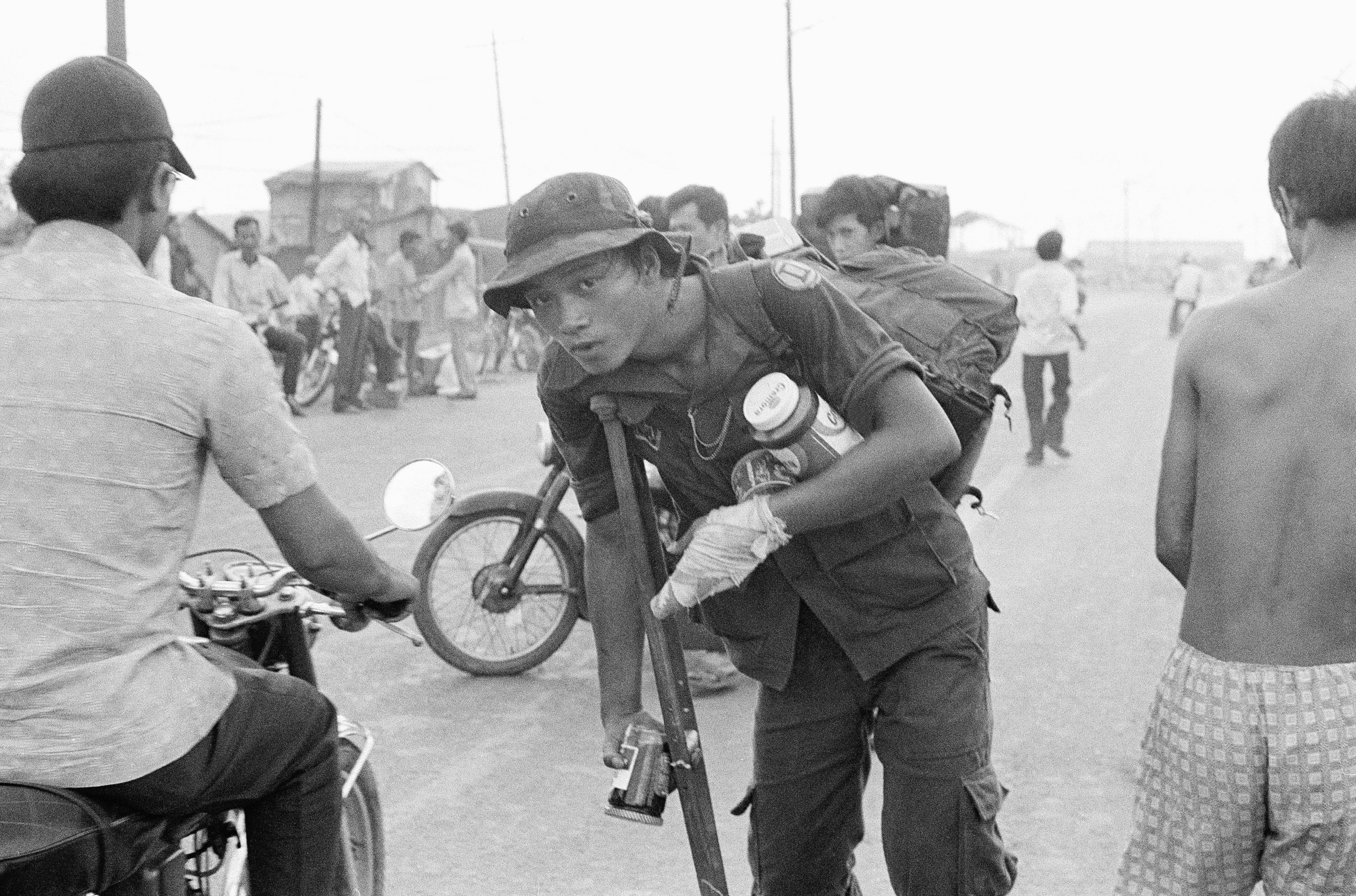 A South Vietnamese war veteran limps away on crutch with food looted from abandoned U.S. installations after evacuation of Saigon, April 29, 1975. (AP Photo)