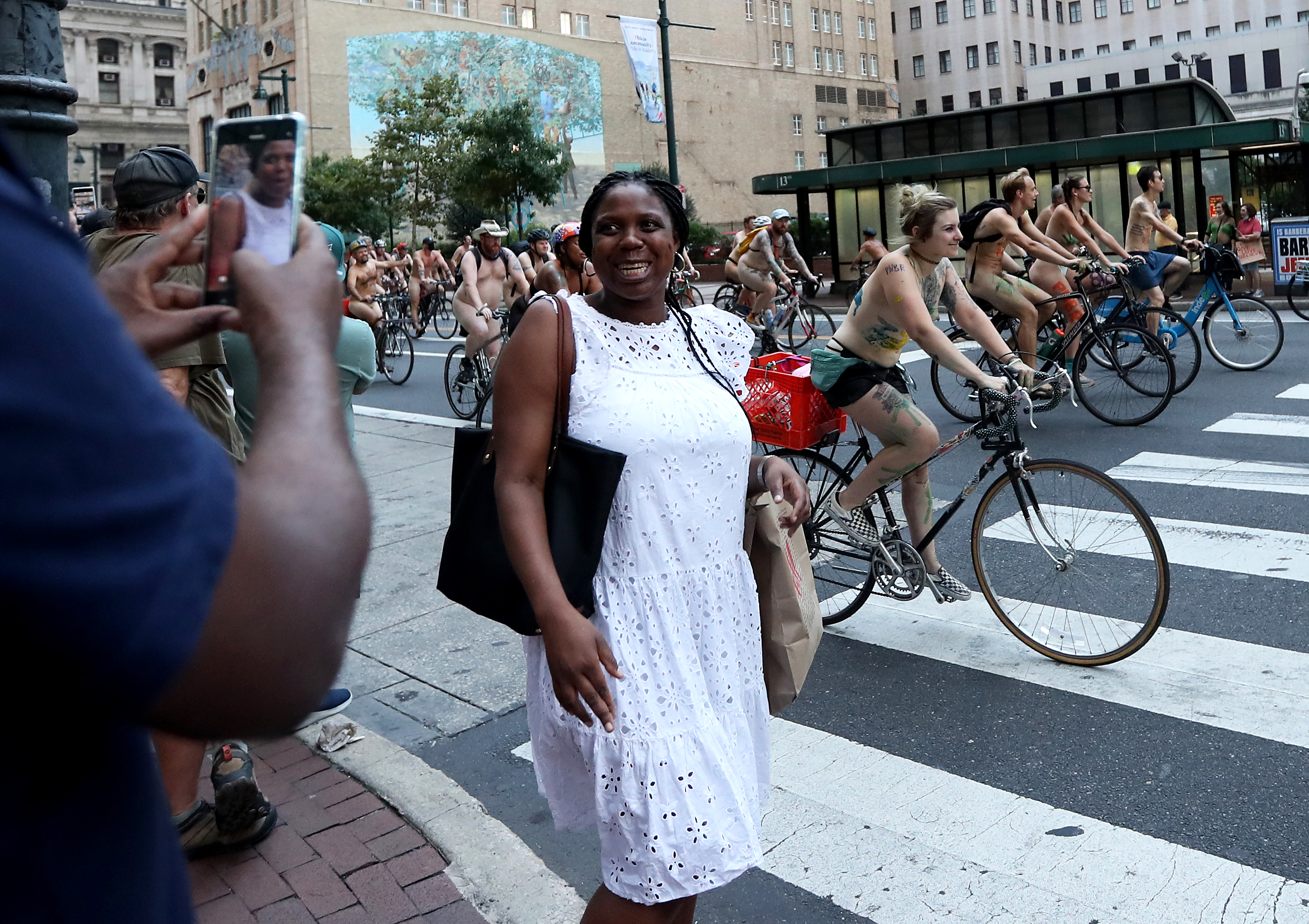 A woman smiles as she has her photo taken while Philly Naked Bike Ride participants ride along Market Street in Philadelphia, Saturday, Aug. 27, 2022.