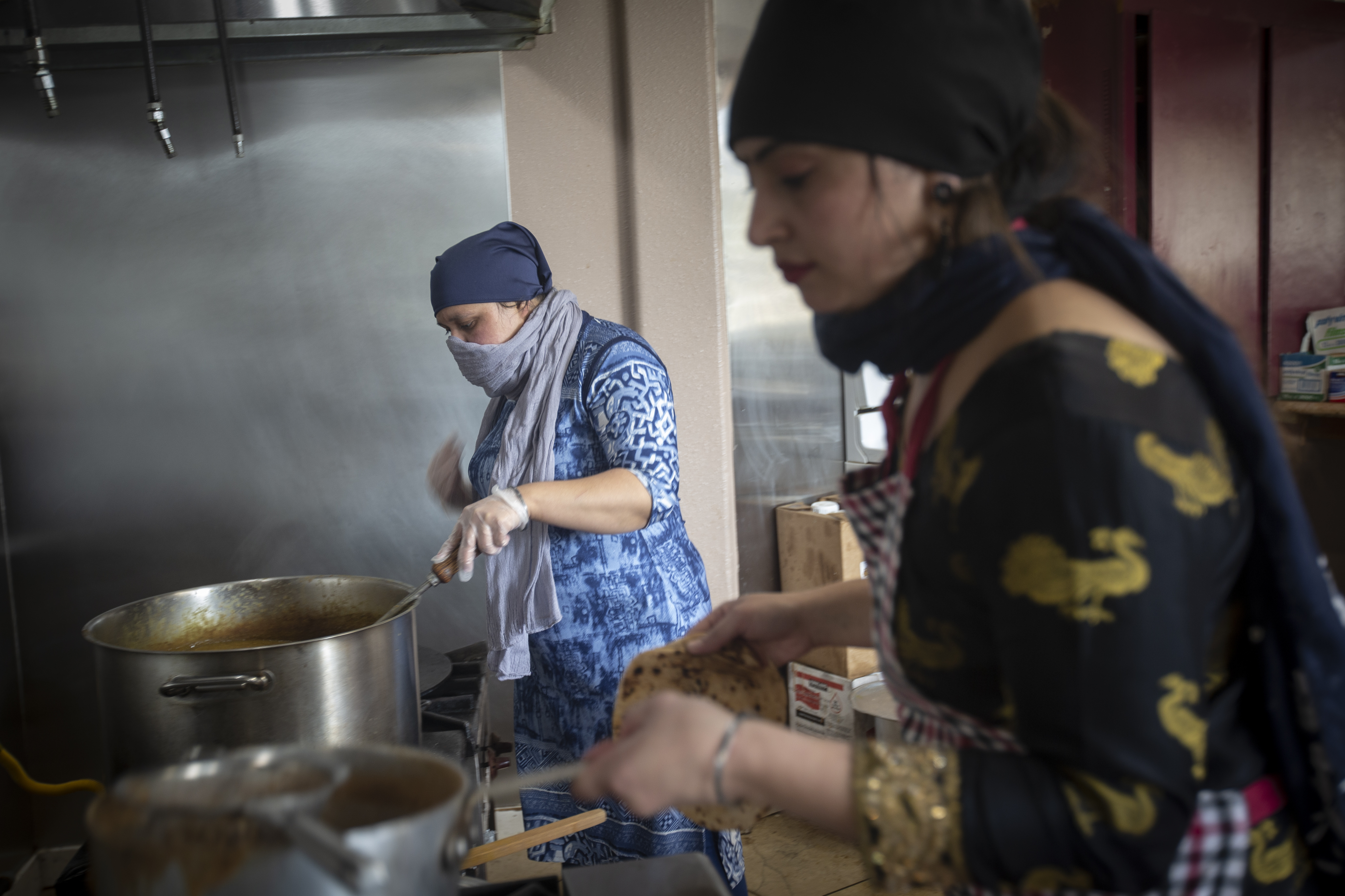 A cook in a Sikh kitchen cooking in an extremely large pot.