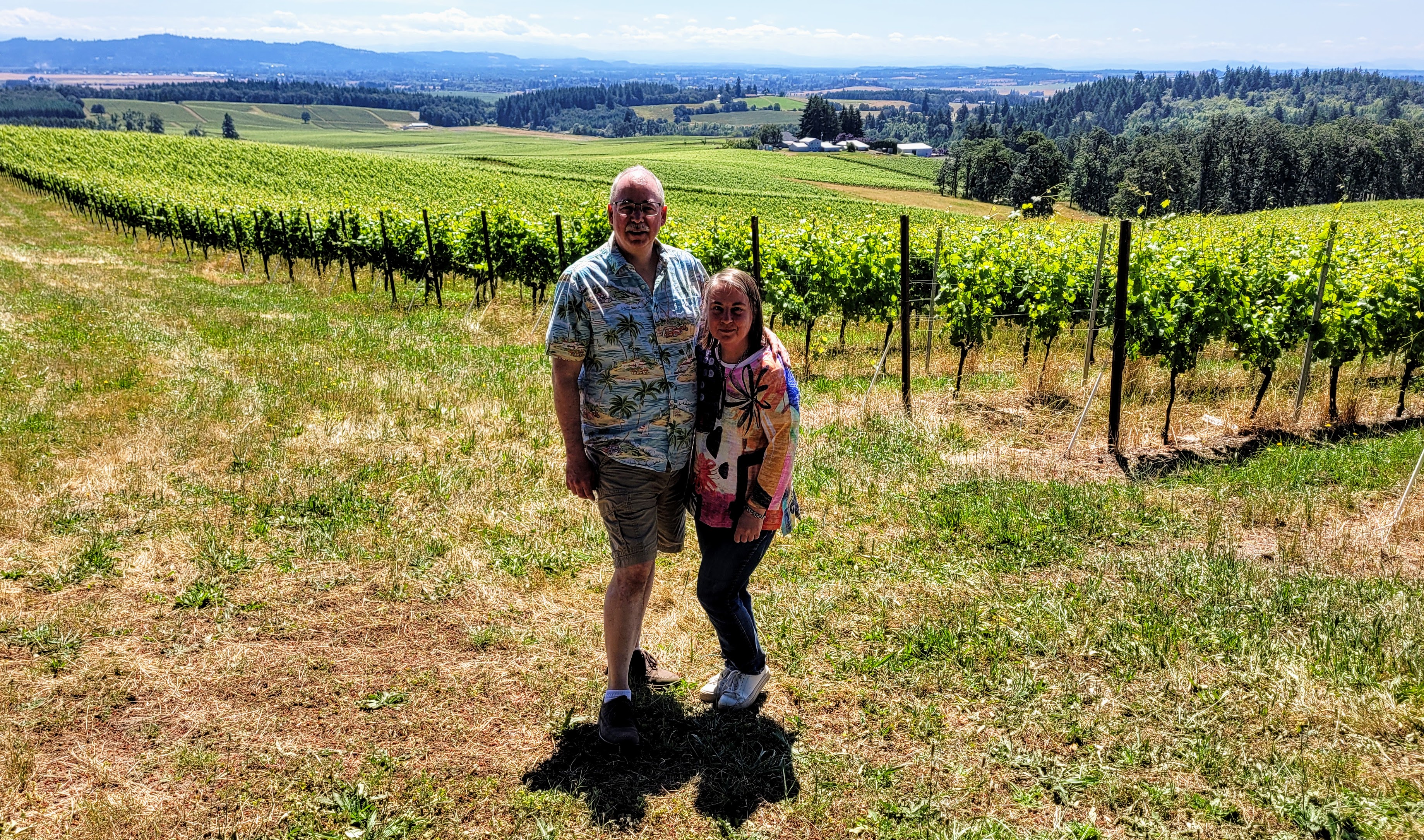 A man and a woman stand in a vineyard.