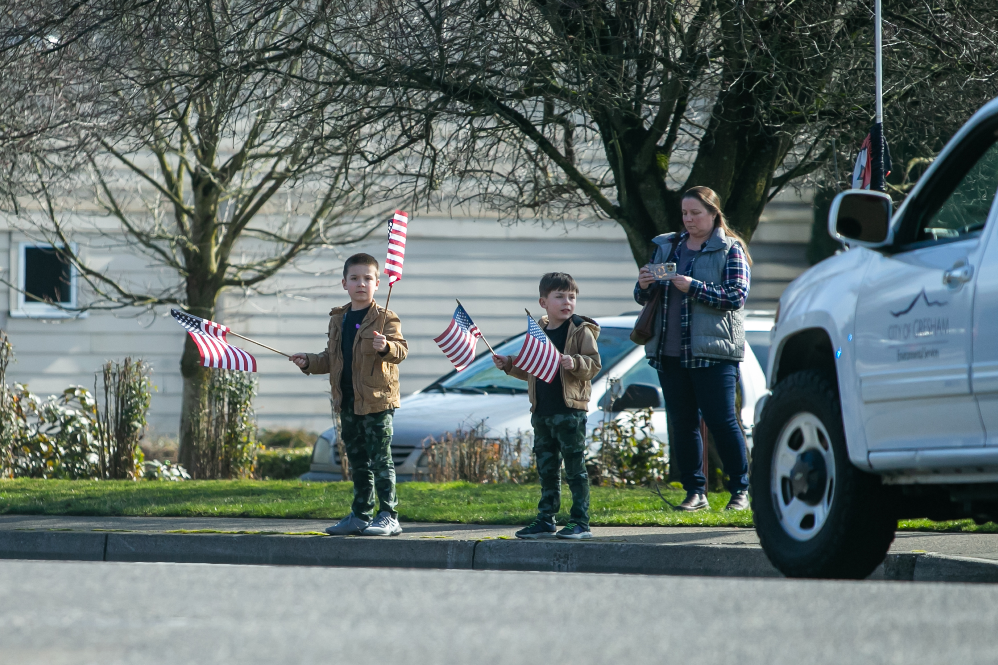 Two young boys wave American flags as a procession of first responders drives through downtown Gresham, Oregon honoring Gresham Firefighter Brandon Norbury on Wednesday, Feb. 15 2023.
