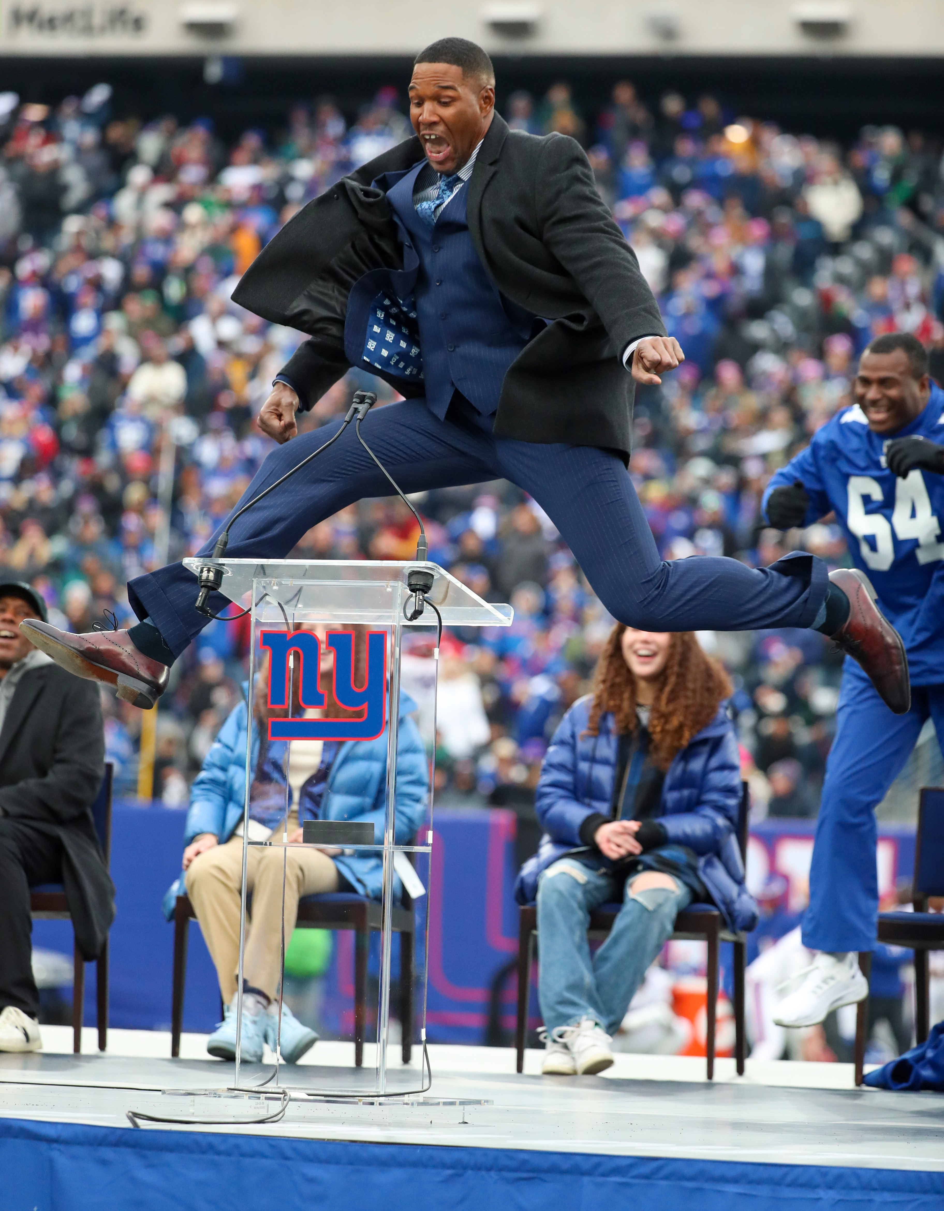 Former New York Giants defensive end Michael Strahan leaps on stage during a halftime ceremony to retire his No. 92 on Sunday, Nov. 28, 2021 at MetLife Stadium.