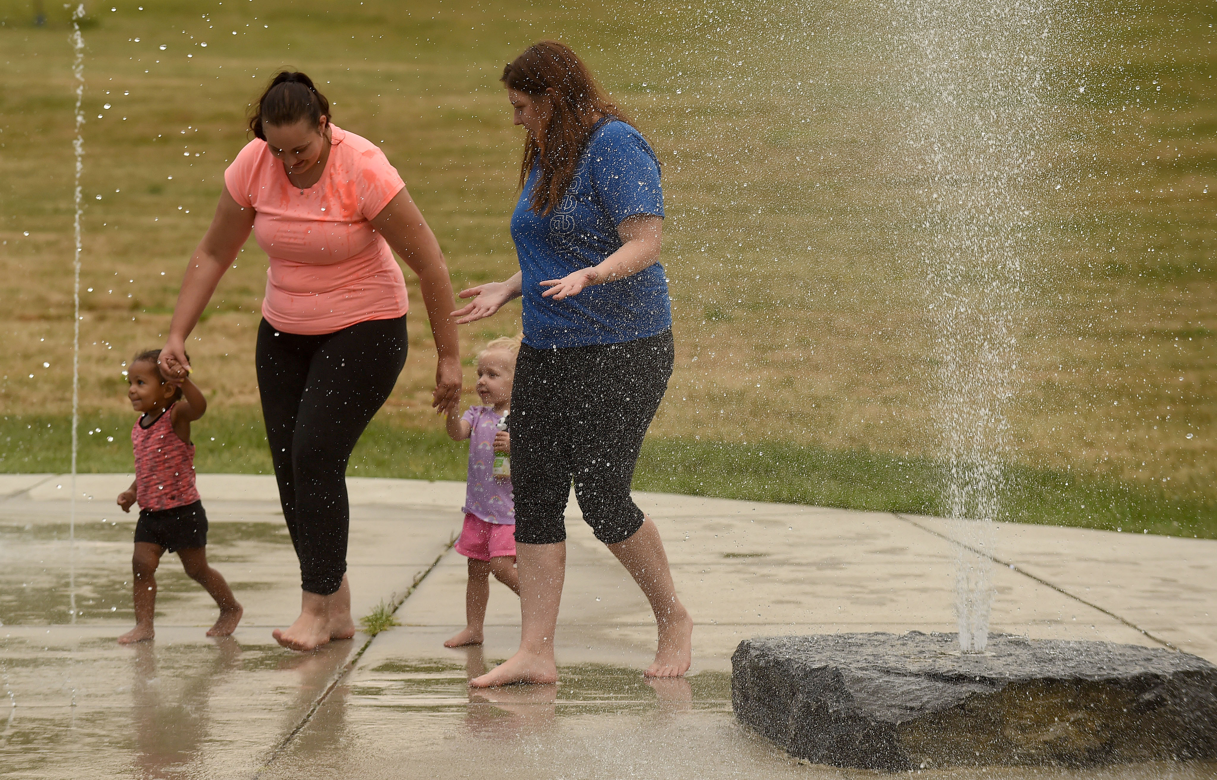 People are still looking for a way to cool down during a heat spell in Syracuse, July 8, 2020.  From left,  Harley Botame 1 1\2 ,  mom Ashley Silvernal, Avalynn Euson 11\2 and mom Shana Lovine walk through the spray area in Lower Onondaga Park.  Dennis Nett | dnett@syracuse.com