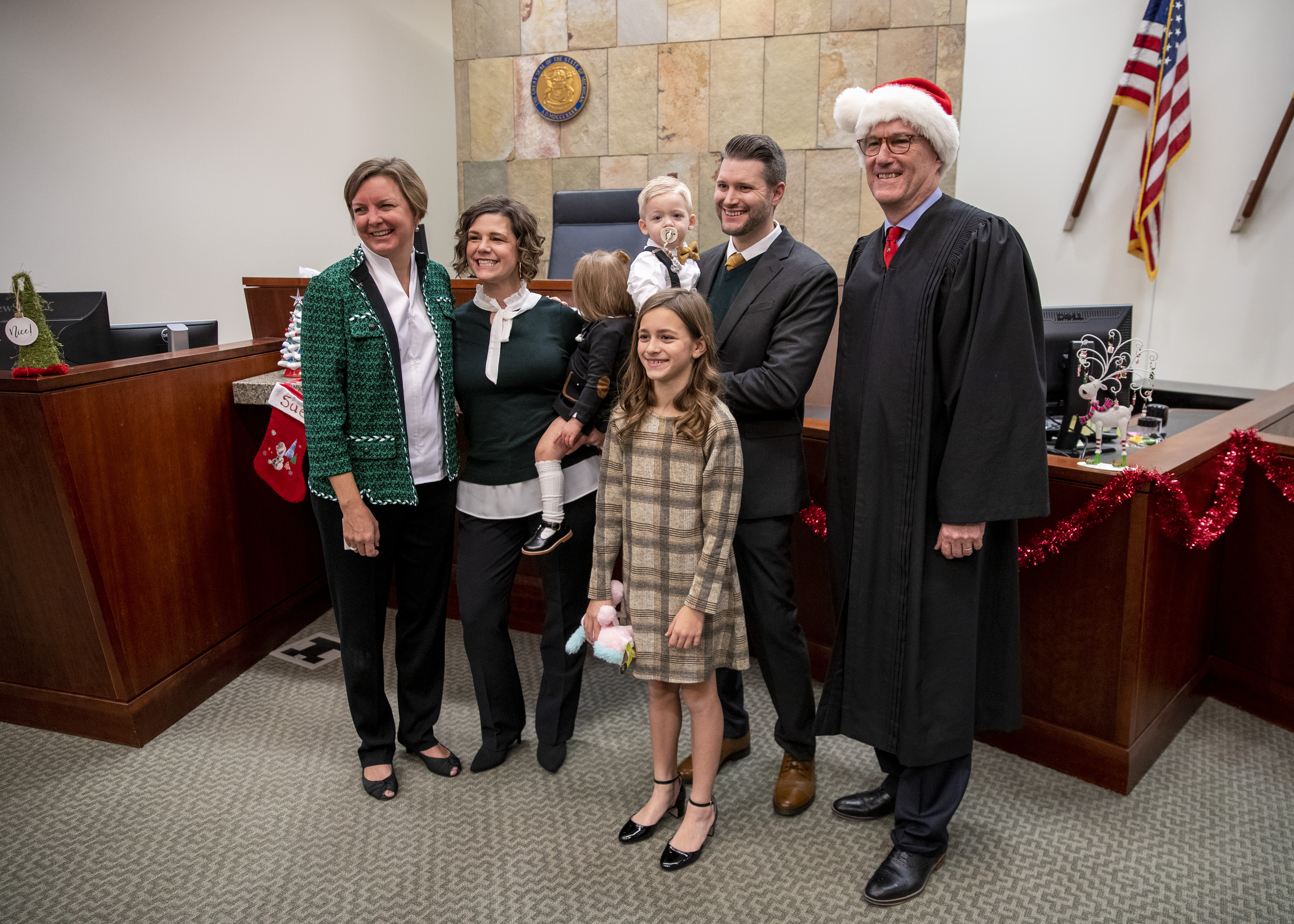 The Myers family poses for pictures with Judge T.J. Ackert, far right, and attorney Melissa Neckers, far left, during Adoption Day at the Kent County Courthouse in Grand Rapids on Thursday, Dec. 8, 2022. Tammy and Jordan Myers are the biological parents of 1-year-old twins Eames, center right, and Ellison. Lauren Vermilye, a surrogate, gave birth to the twins after Tammy went through breast cancer treatment and has no claim to the babies. The Myers family was able to adopt the twins after convincing the court system to grant them custody. Also pictured is their daughter, Corryn Myers, 10.(Cory Morse | MLive.com)