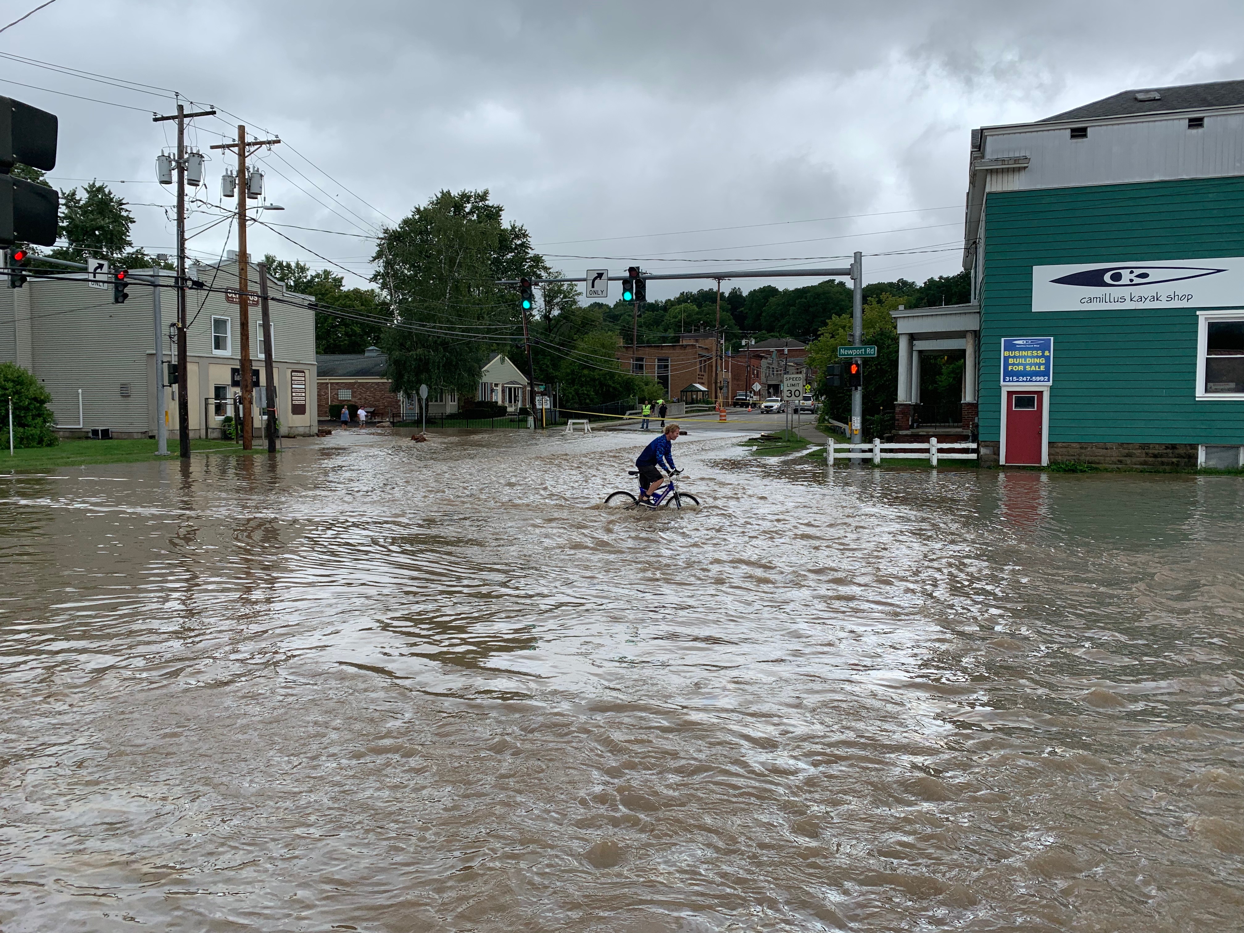 A person rides a bike through flood waters at Newport and South streets in Camillus on Thursday, Aug. 19, 2021.