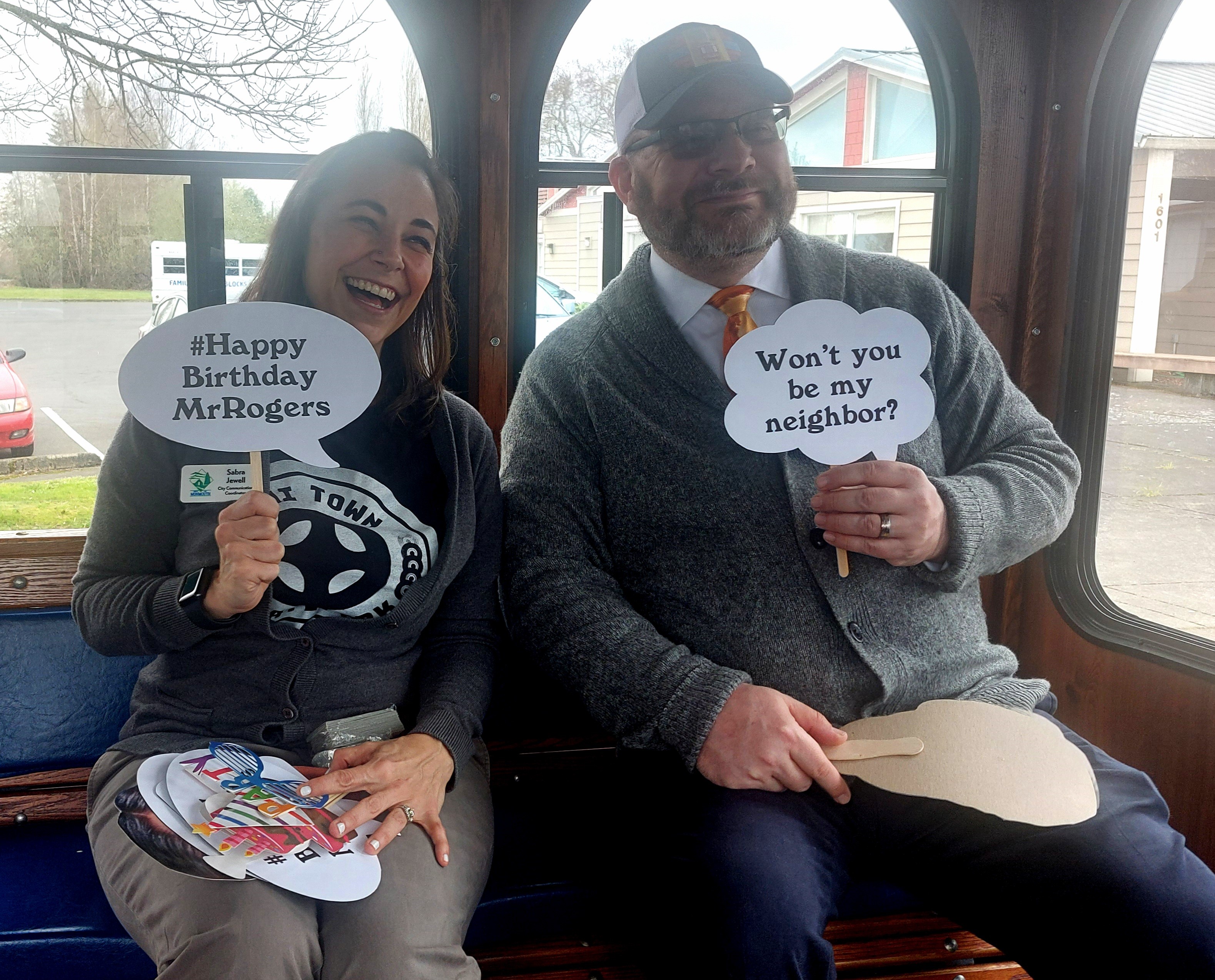 Sabra Jewell and Kevin Parks sit inside the trolley holding signs that say happy birthday mr. rogers and won't you be my neighbor