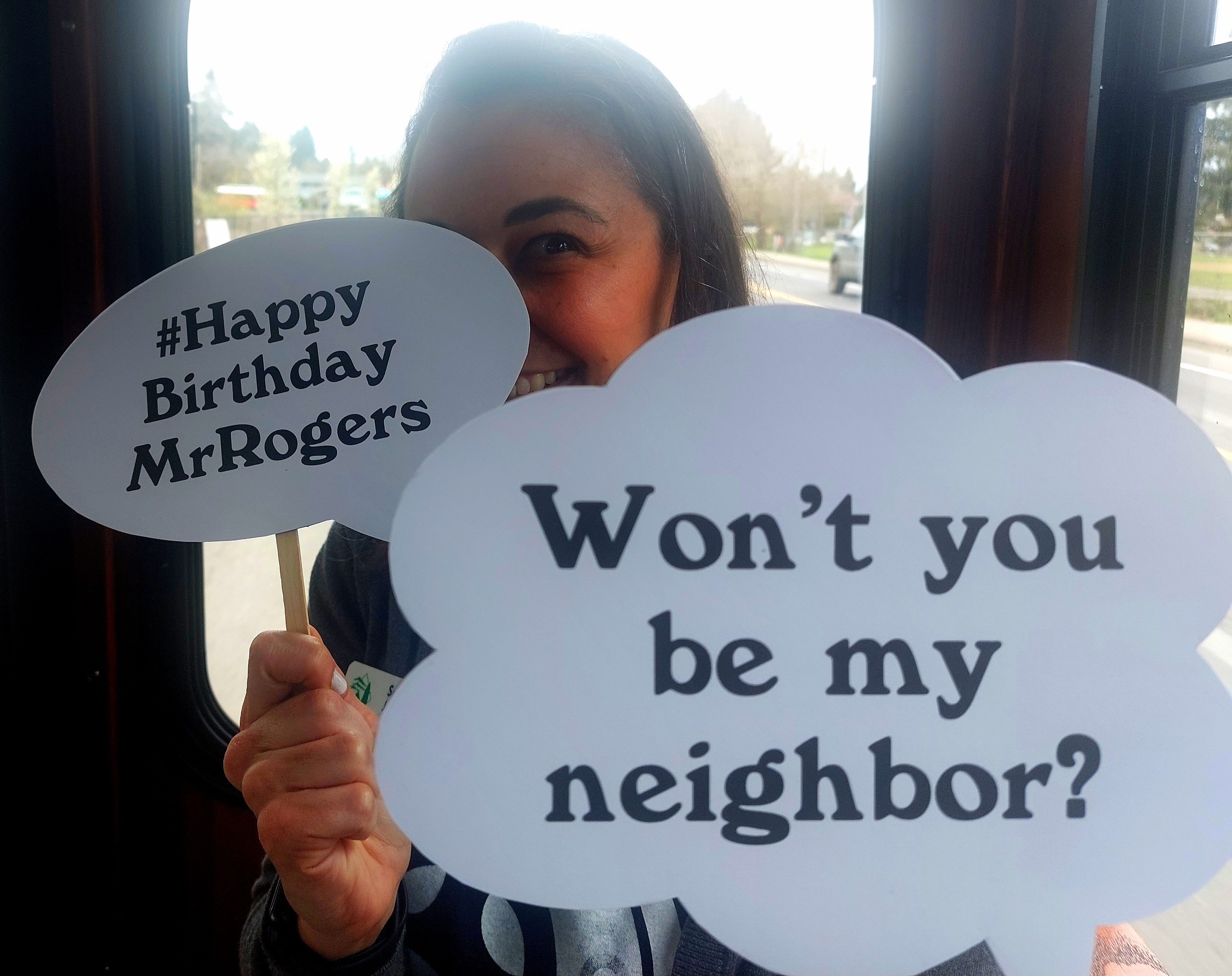 Sabra Jewell holds signs that say Won't you be my neighbor? and Happy Birthday MrRogers
