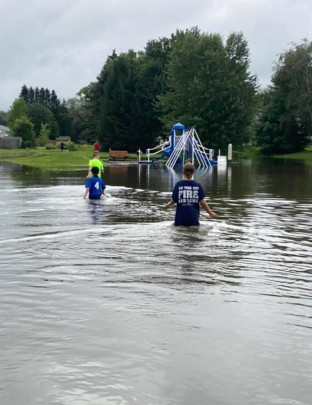 People wade through waist-deep water at a playground in the Willowstream neighborhood in Clay, N.Y. Photo by Kayleigh Barrett