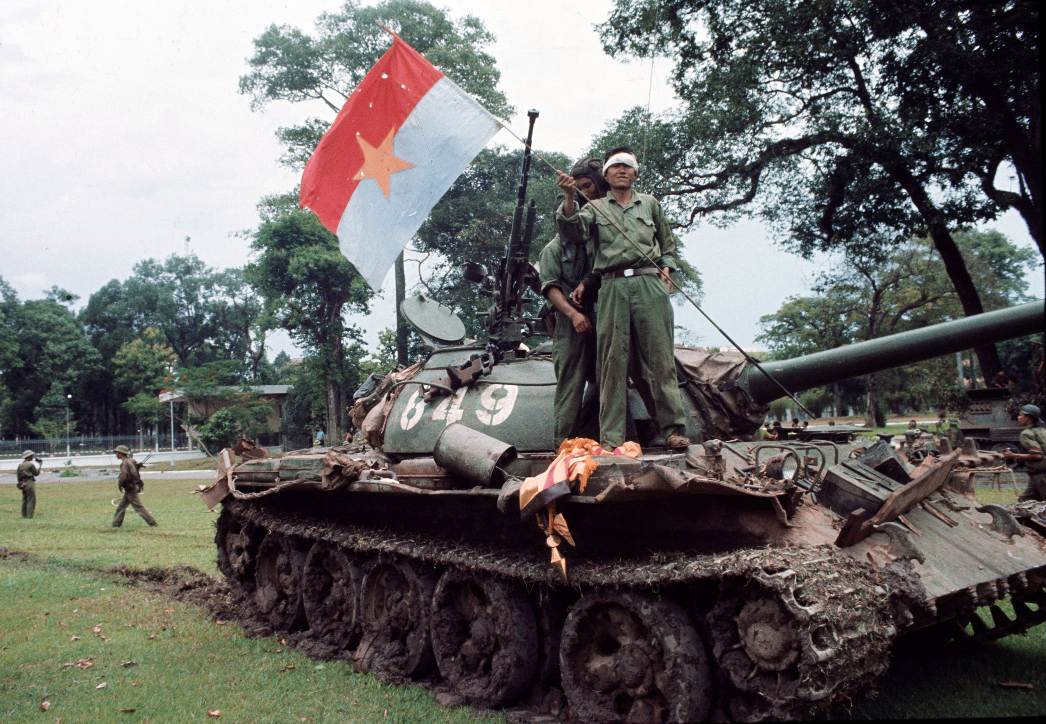With a South Vietnamese flag at his feet, a victorious North Vietnamese soldier waves a communist flag from a tank outside Independence Palace in Saigon, April 30, 1975, the day the South Vietnamese government surrendered, ending the Vietnam War. (AP Photo/Yves Billy)