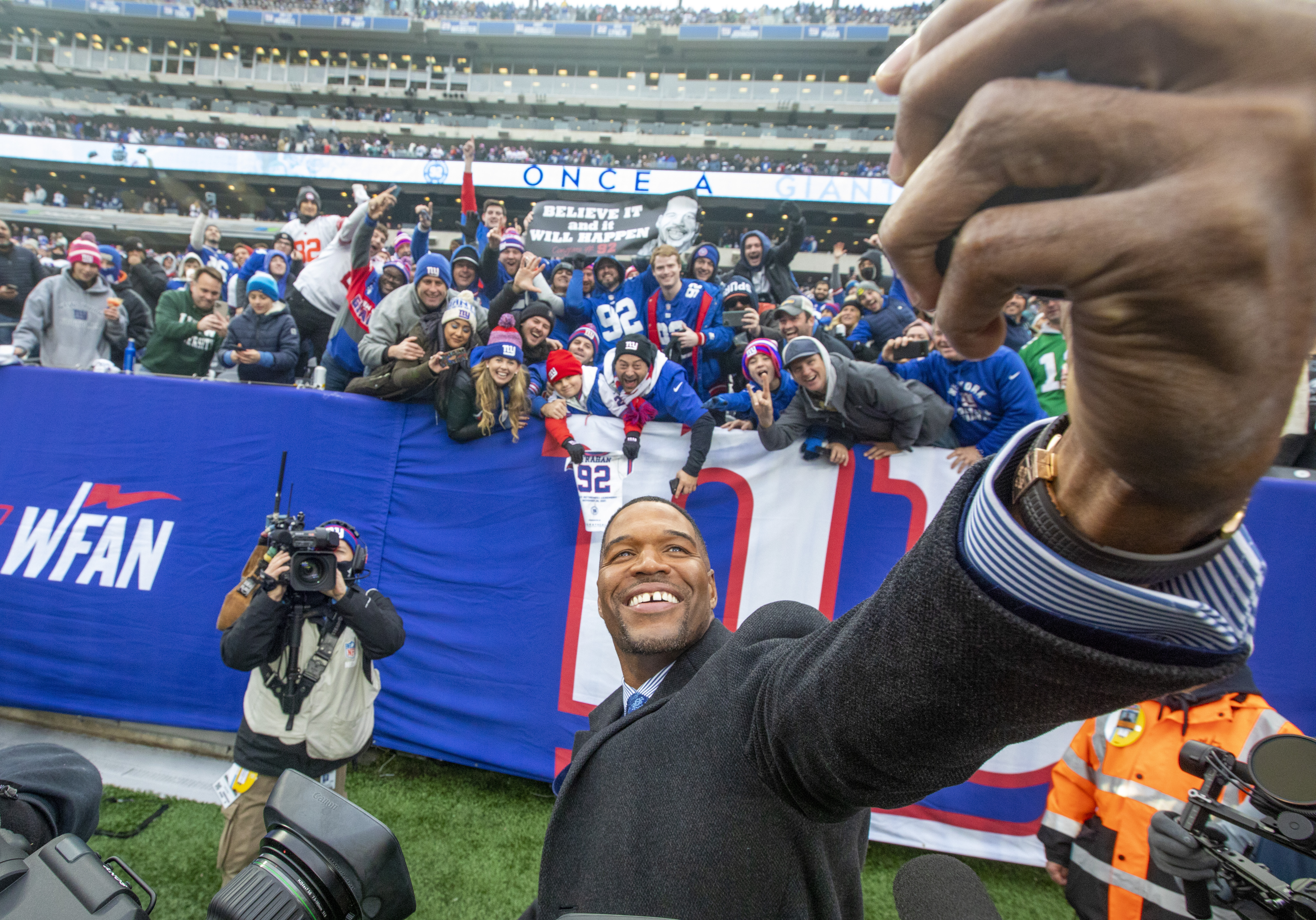 Former New York Giants defensive end Michael Strahan takes a selfie with fans holding a sign that reads, ‘Believe it and it will happen’ after a halftime ceremony to retire his No. 92 on Sunday, Nov. 28, 2021 at MetLife Stadium.