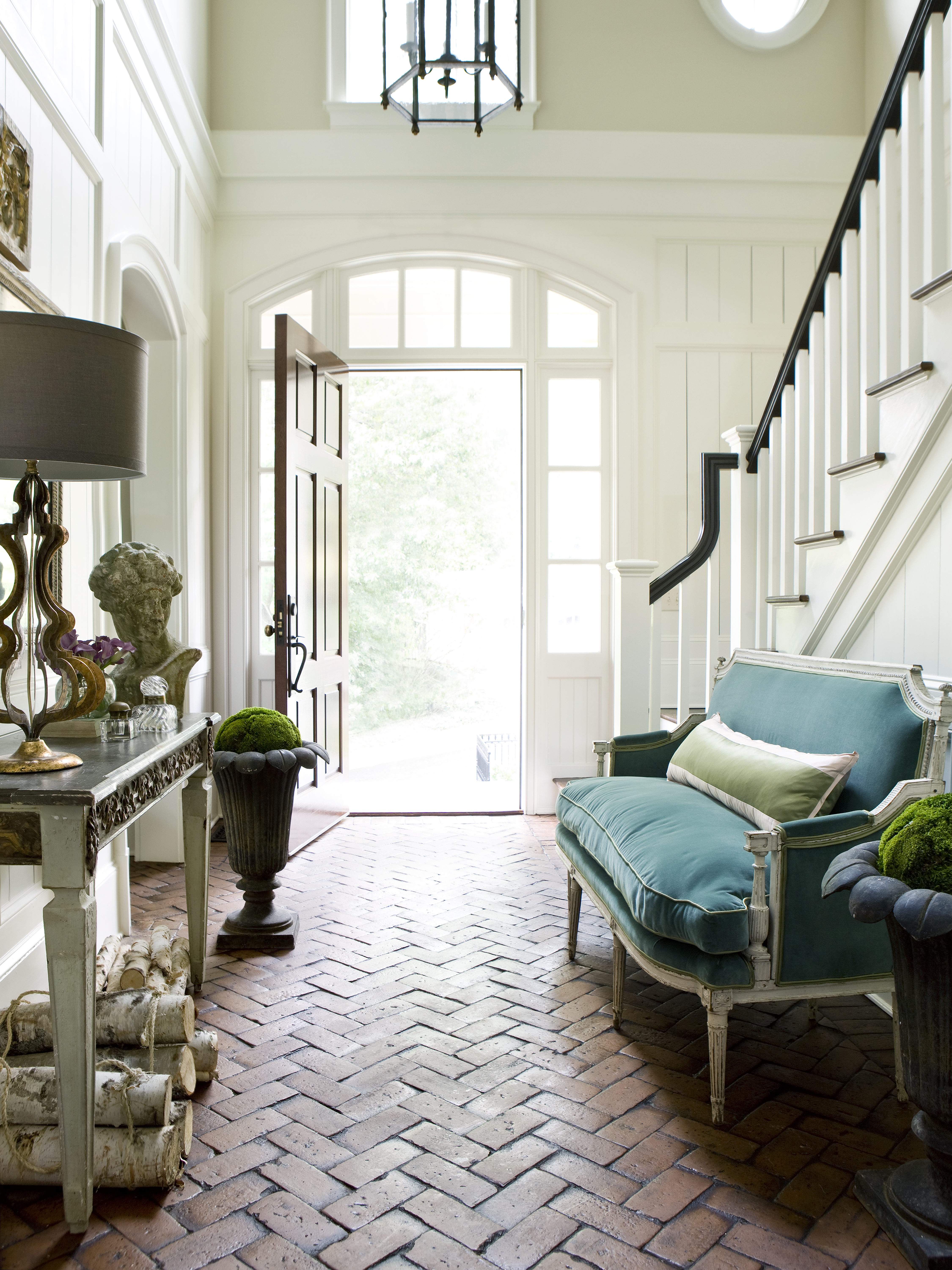 "The antique settee in an updated vibrant colored velvet welcomes a guest to sit and drop their handbag or jacket.  The texture of the brick, wall paneling, fabrics and antiques give the guest so much to take in and enjoy upon entering the house!" according to Amy Morris Interiors. Courtesy of Erica George Dines