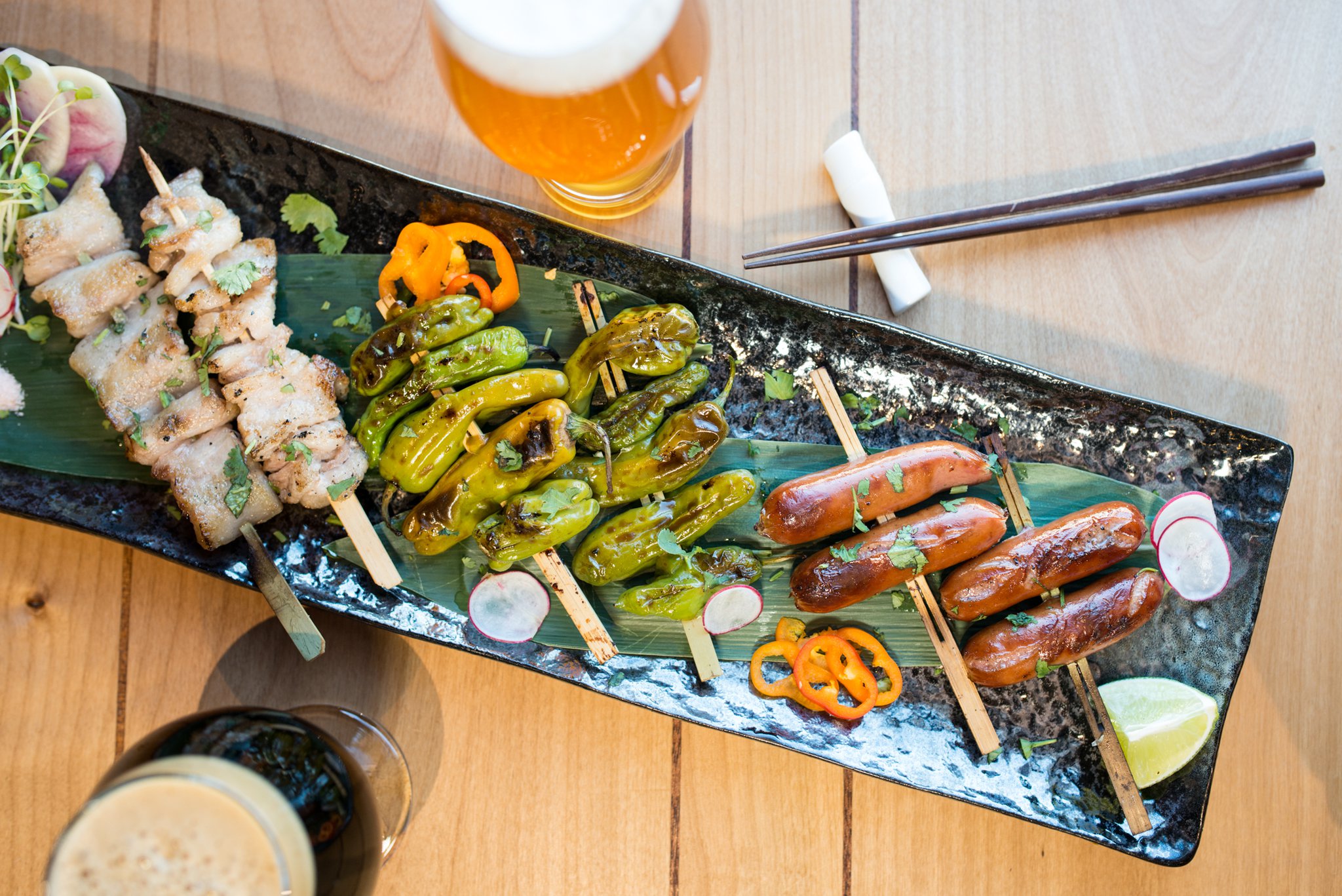 Hopstix Robatayaki plate with Silky Pork Belly, Shishito Peppers, and Kurobuta Sausage. Pictured with Wrecking Bar Jemmy Stout and Max Lager's Hopslosion. Photo credit- Mia Yakel.