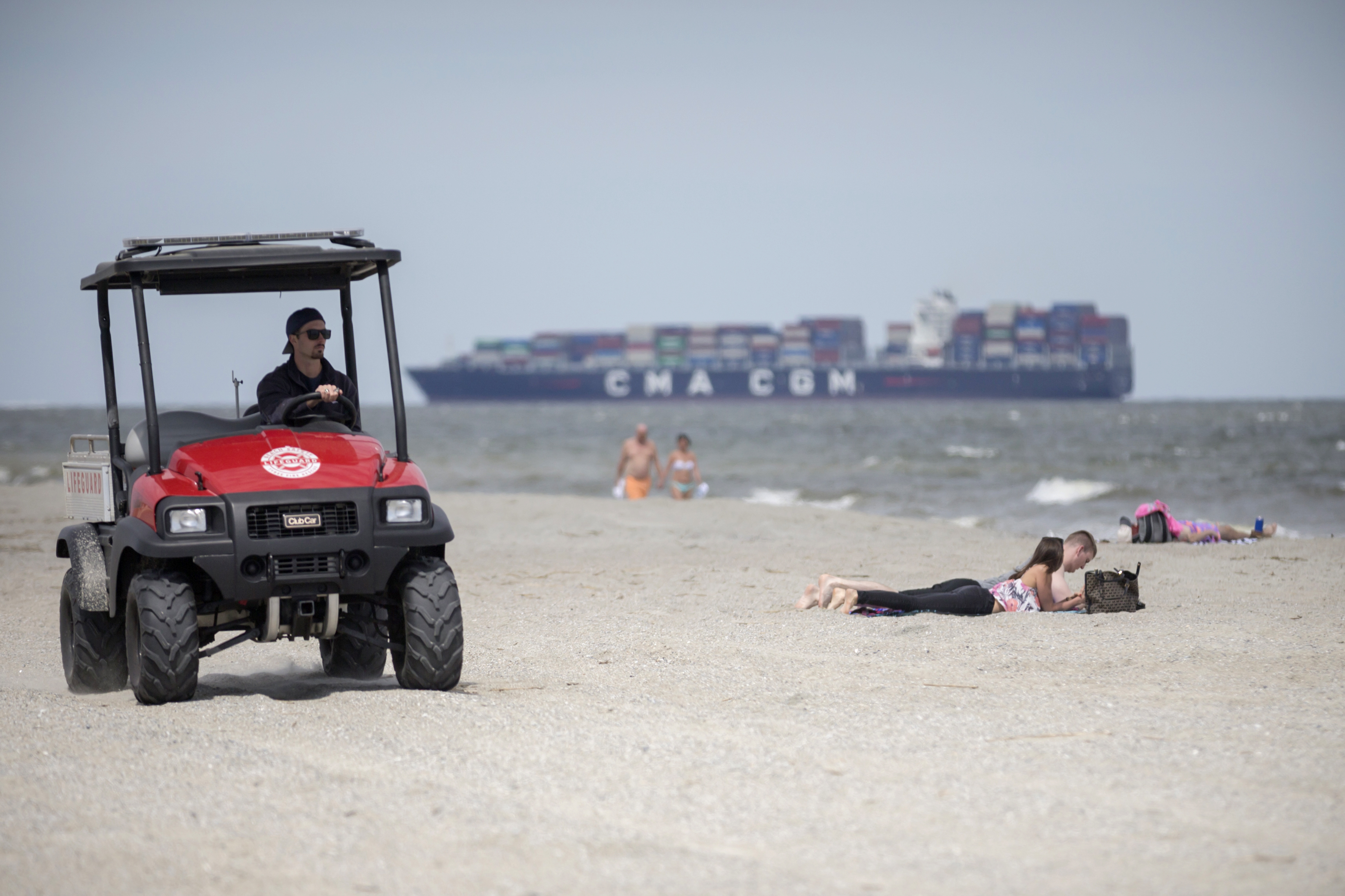 A member of the Tybee Island Life Guards patrols the beach on a ATV while visitors sunbathe in the sand on Saturday, April 4, 2020. (Photo: Stephen B. Morton/Special to the AJC)