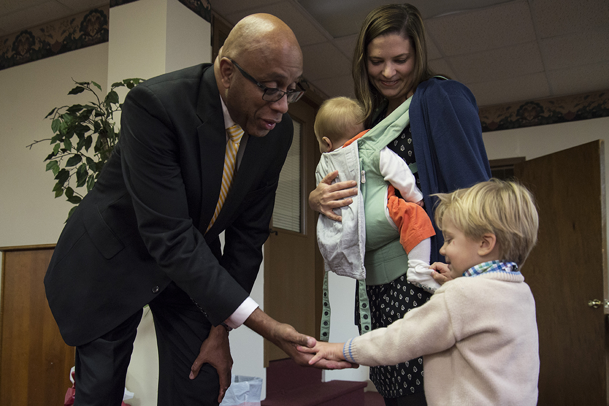 Pastor James Goolsby of First Baptist Church on New Street gives Billy a high five while his mother, Audrey Dickison, watches with her youngest son, Mac, in her arms on Sunday, Nov. 19 at First Baptist Church's Thanksgiving Potluck. Dickison is the wife of Scott Dickison, the reverend at First Baptist Church of Christ on High Place. (Jenna Eason / for the AJC)