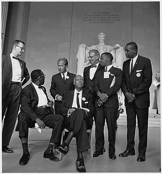 A 23-year-old John Lewis (second from the right), then chairman of the Student Nonviolent Coordinating Committee, was the youngest speaker at the March on Washington. Others shown are from left: Mathew Ahmann, executive director of the National Catholic Conference for Interracial Justice; (seated with glasses) Cleveland Robinson, chairman of the Demonstration Committee; (beside Robinson is) A. Philip Randolph, organizer of the demonstration and veteran labor leader who helped to found the Brotherhood of Sleeping Car Porters, American Federation of Labor (AFL), and a former vice president of the American Federation of Labor and Congress of Industrial Organizations (AFL-CIO); (standing behind the two chairs) Rabbi Joachim Prinz; (wearing a bow tie and standing beside Prinz) is Joseph Rauh Jr., a Washington, D.C., attorney and civil rights, peace and union activist; and Floyd McKissick, national chairman of the Congress of Racial Equality.