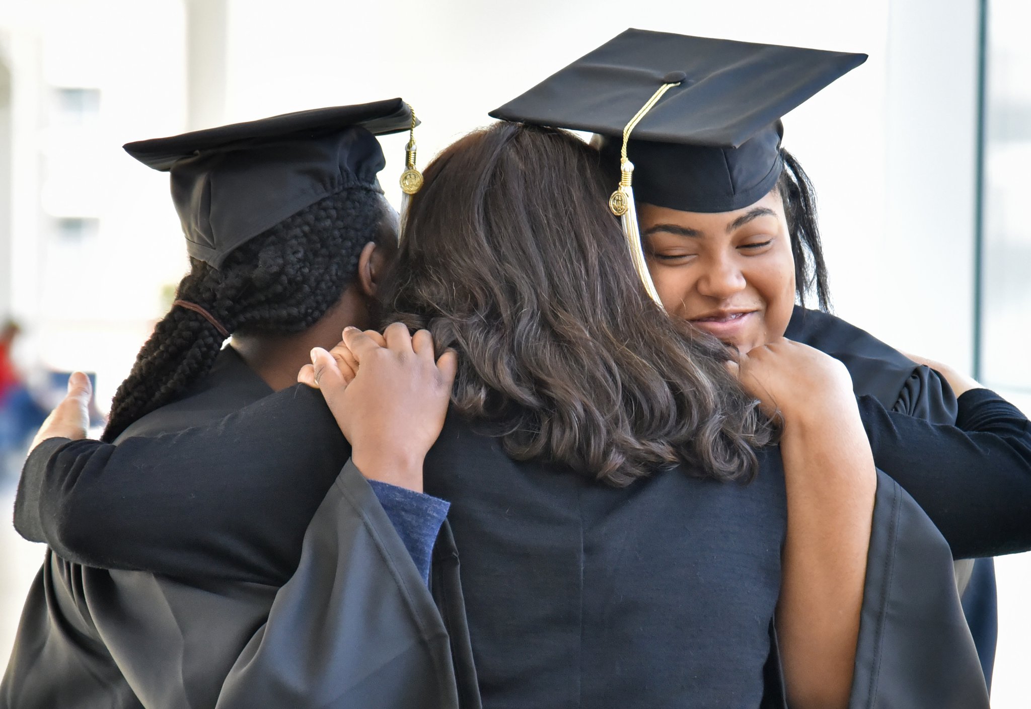Carrie Crayton, left, and Natalie Jackson (right), both from the first graduating class of Georgia Tech’s EXCEL program for students with intellectual disabilities, get a hug from Rene Reese, right, career development coordinator, after they try on their caps and gowns.