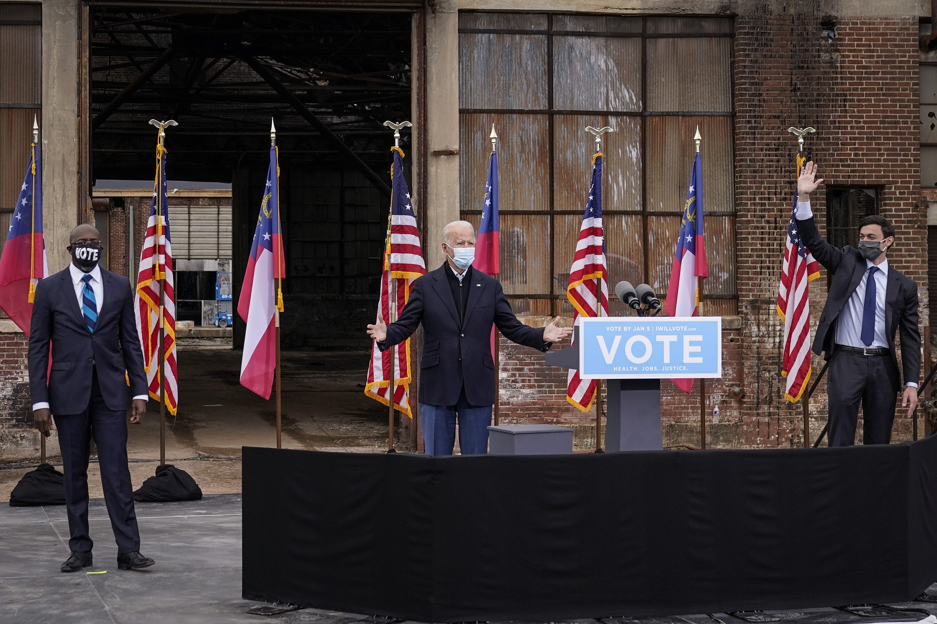 Flanked by Democratic U.S. Senate candidates Rev. Raphael Warnock, left, and Jon Ossoff, U.S. President-elect Joe Biden gestures to the crowd at the end of a drive-in rally at Pullman Yard on December 15, 2020 in Atlanta, Georgia. (Drew Angerer/Getty Images/TNS)