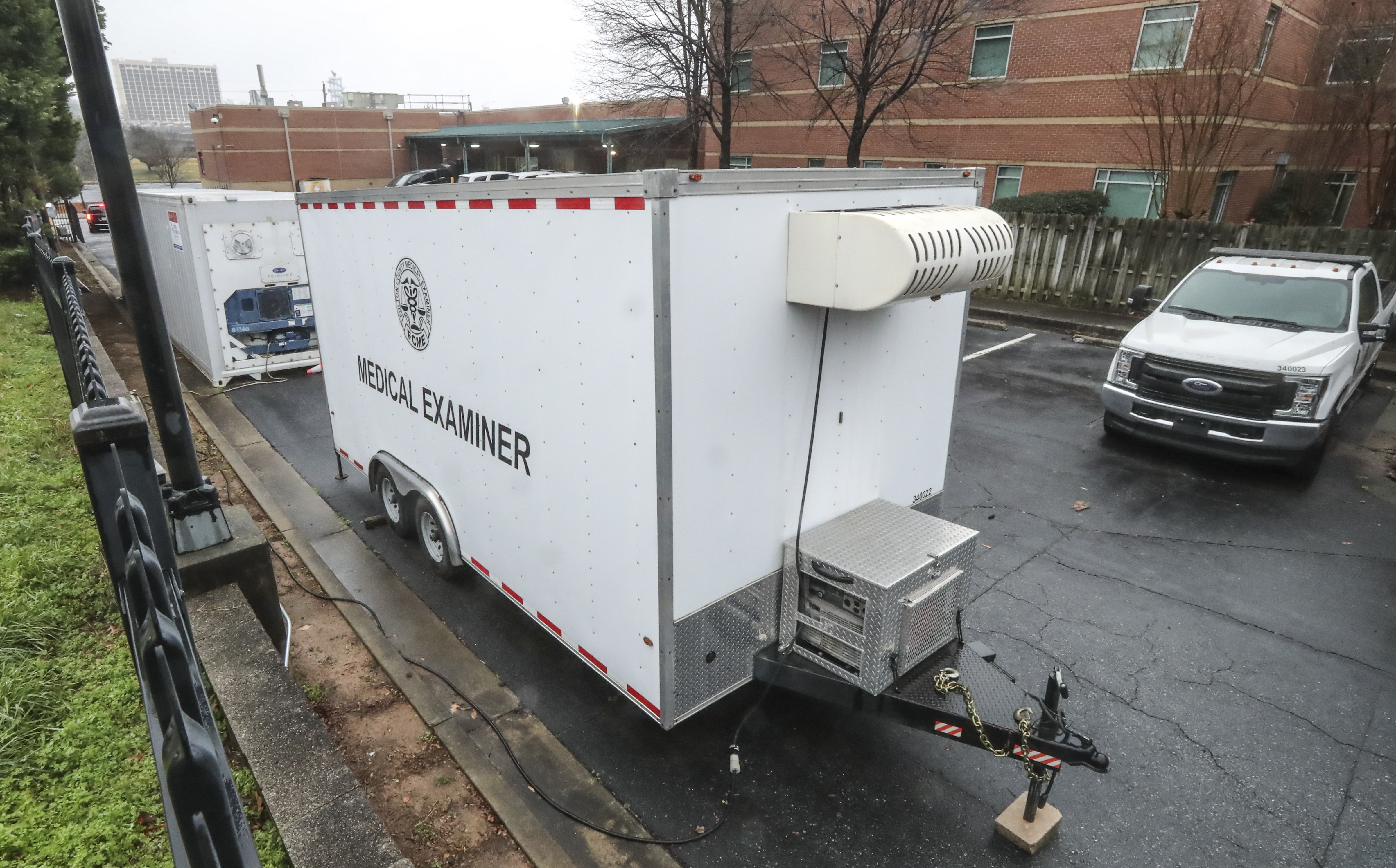 Two marked trailers sit parked outside the Fulton County Medical Examiner's Office. With COVID-related deaths mounting, the office has deployed a refrigerated morgue truck to store bodies, with a second truck ready to go. (John Spink / John.Spink@ajc.com)