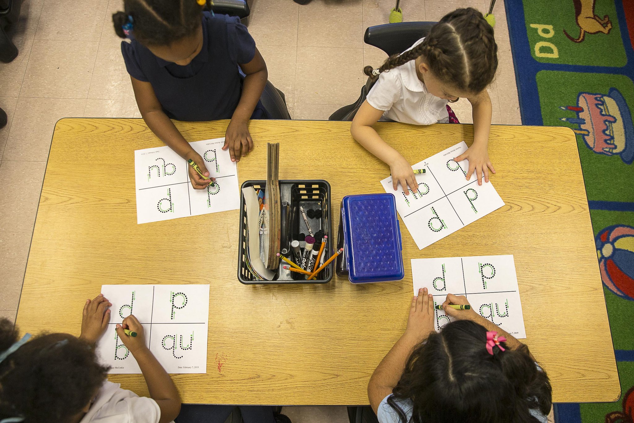 Kindergarten students trace letters and digraphs onto a plastic gridded sheet during their phonics lesson at Benteen Elementary School in Atlanta. The plastic grid is used as a sensory tool to help students remember their lesson.