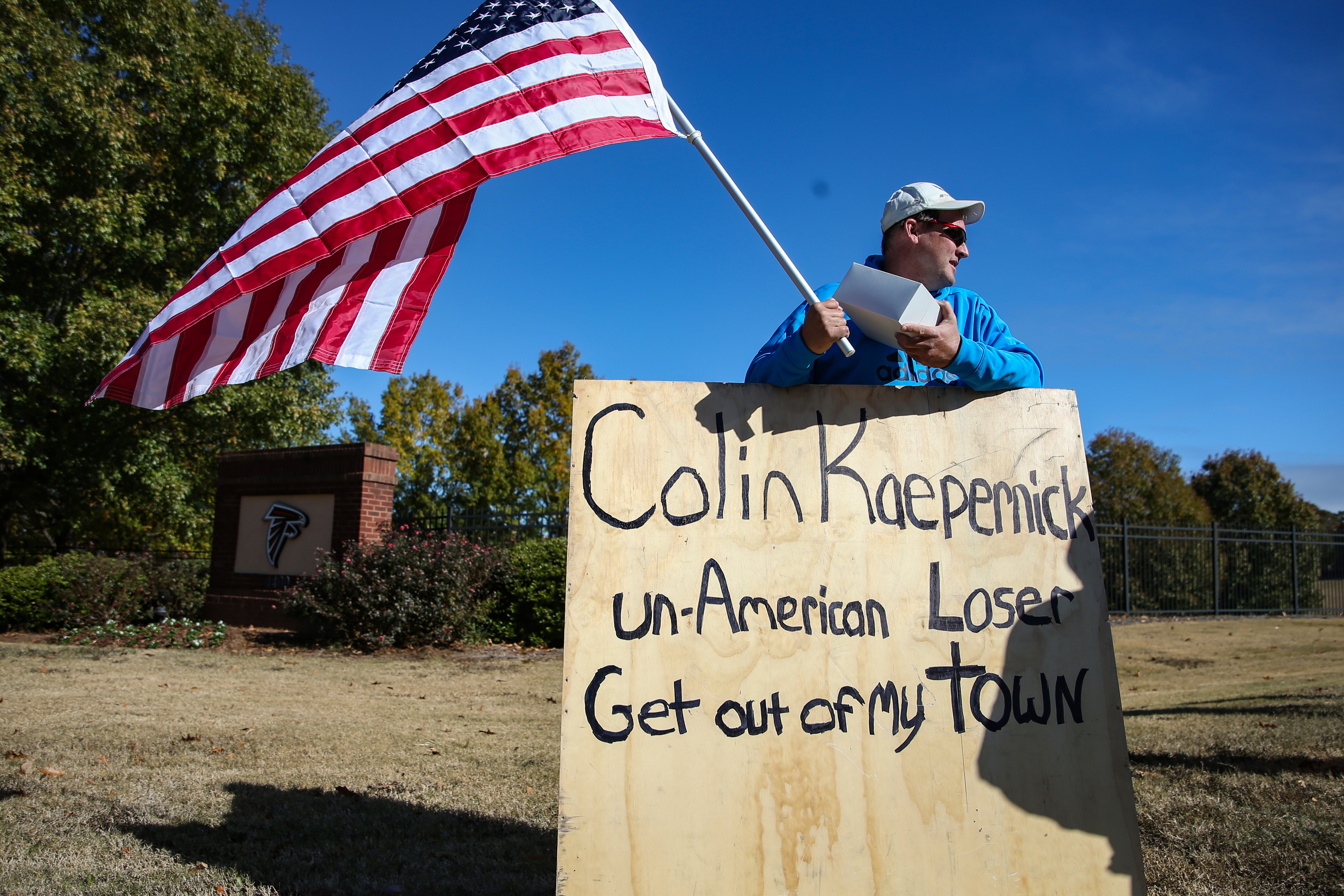 A protester holds an American flag and a sign outside of the Atlanta  Falcons' training facility where free agent quarterback Colin Kaepernick  was set to workout for NFL football scouts, Saturday, Nov.