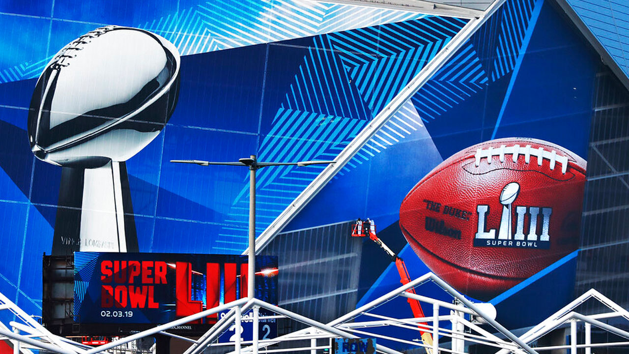 In this Jan. 17, 2019 photo, workers use a lift to install a Super Bowl 53 wrap on the outside of Mercedes-Benz Stadium as it is transformed for the big NFL football game in Atlanta.