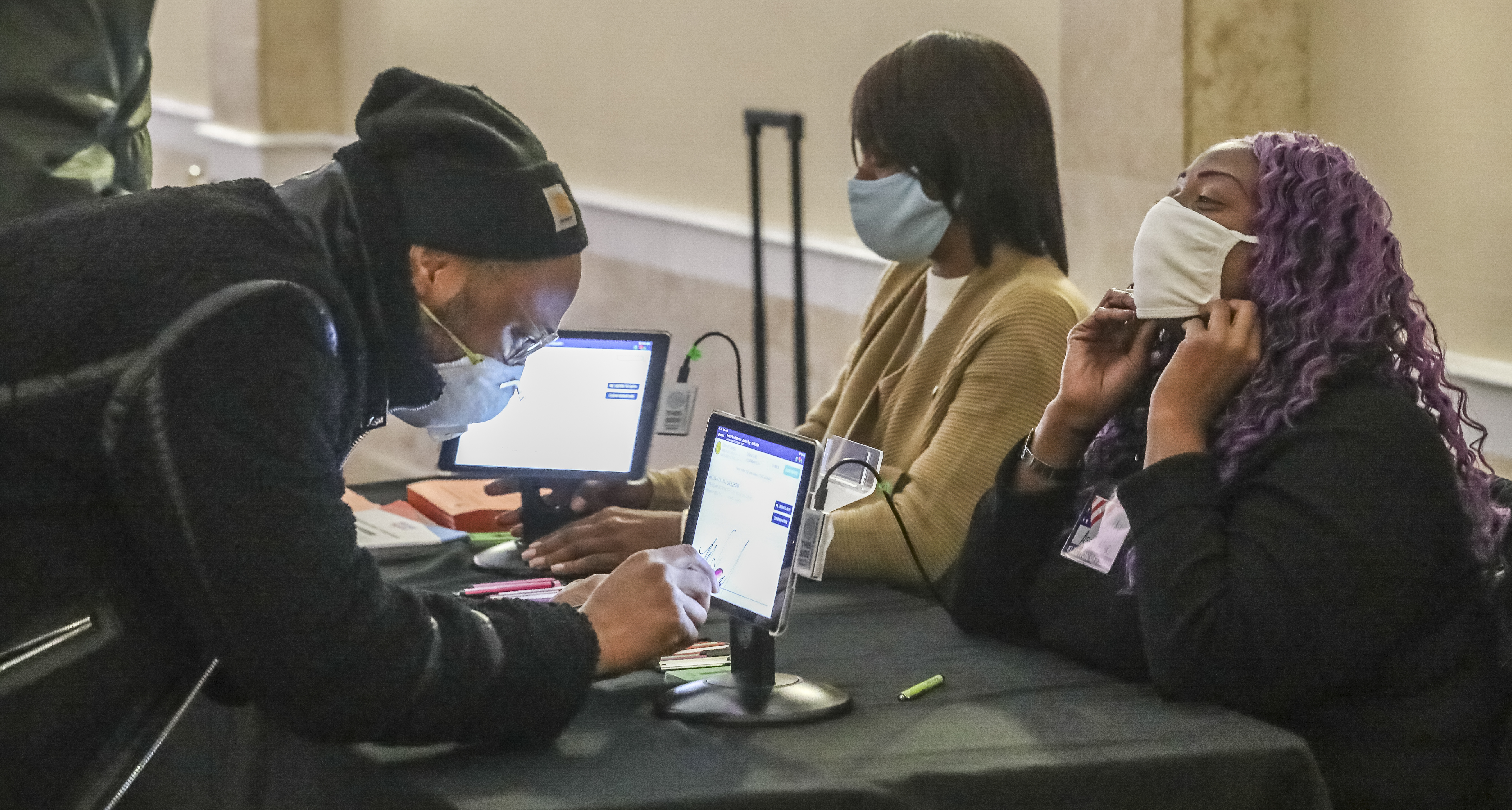 Kamal Gillespie, left, verifies his voter ID information to poll workers Brandy Allen (center) and Cuedriene Edwards on Tuesday at the Park Tavern in Atlanta. (John Spink / John.Spink@ajc.com)