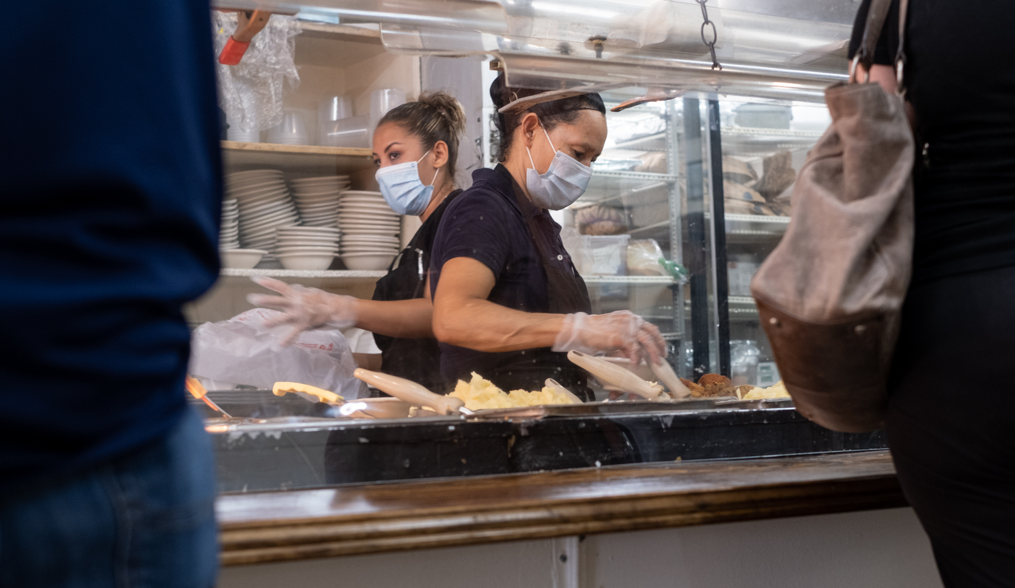 200717-Tucker-Ingred Cruez, left, and Marie Rodriguez help customers from behind acrylic panels during the lunch rush at Matthews Cafeteria on Main Street in Tucker on Friday afternoon July 17, 2020. The dining institution, established in 1955, ask customers to wear masks, added the acrylic dividers, made separate entrance and exit doors and have drive-up service. Ben Gray for the Atlanta Journal-Constitution