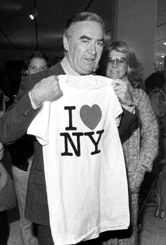 FILE - In this Oct. 9, 1977 file photo, New York Gov. Hugh Carey holds up an "I Love New York" t-shirt during the "I Love New York Fall Festival" in Albany's South Mall. Milton Glaser, the designer who created the "I (HEART) NY" logo and the famous Bob Dylan poster with psychedelic hair, has died. He died Friday, his 91st birthday. (AP Photo, File)