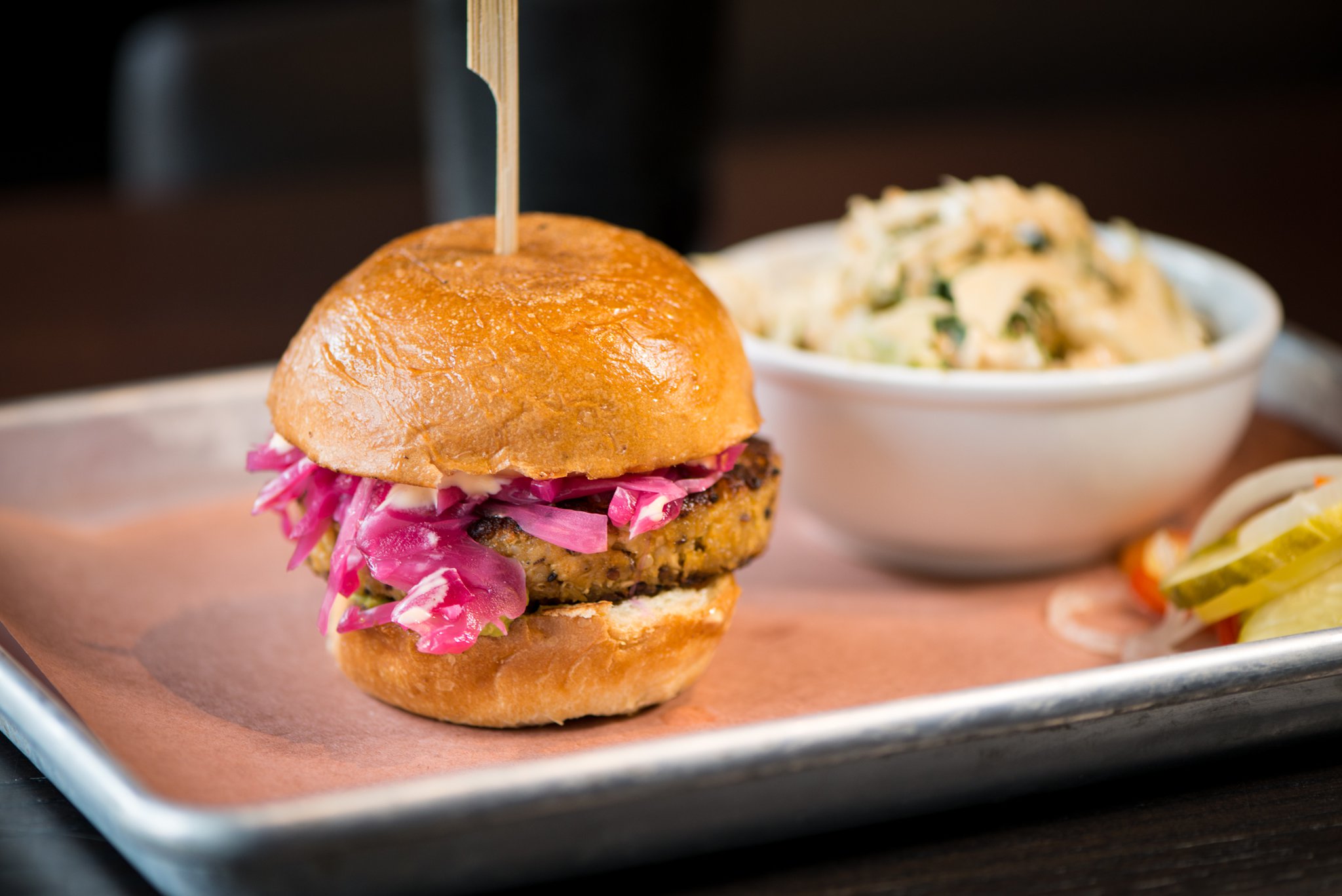 Cauliflower Sandwich, a hand-made cauliflower patty topped with avocado smash, house-made pickled cabbage and sriracha aioli on a toasted bun. Photo credit- Mia Yakel.