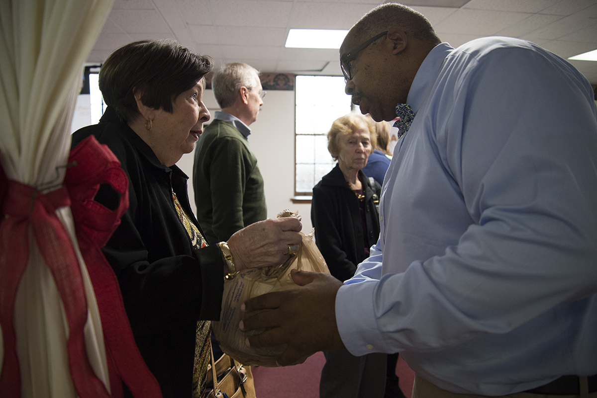 Lillian Rice, of First Baptist Church of Christ on High Place, hands the food she brought to Jimmie Smith, a deacon at First Baptist Church on New Street, at First Baptist Church's Thanksgiving Potluck on Sunday, Nov. 19. (Jenna Eason / for the AJC)
