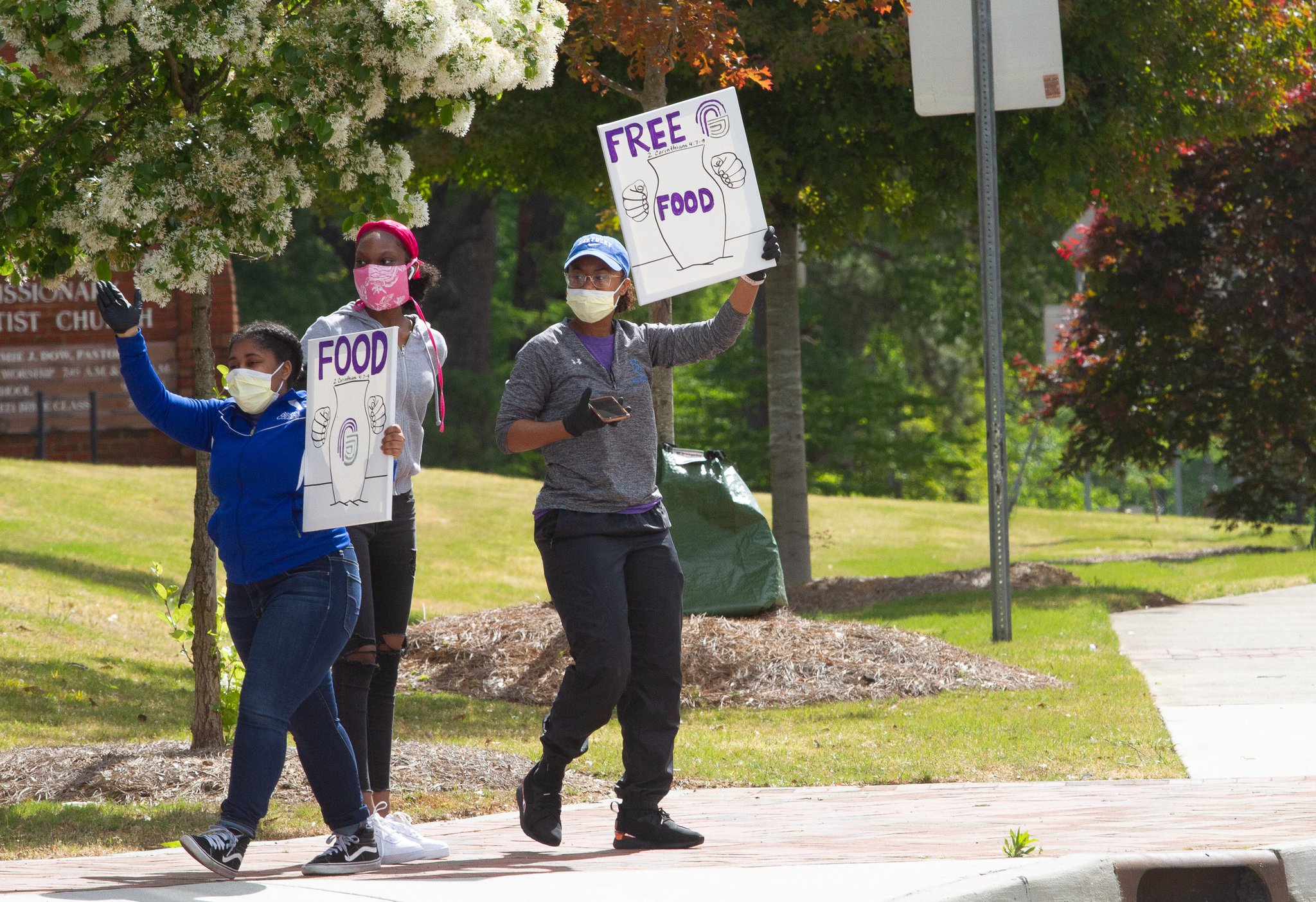 Members of the Pleasant Grove Baptist Church in Marietta hold signs telling motorists about the church's food giveaway Saturday, April 18, 2020. STEVE SCHAEFER / SPECIAL TO THE AJC