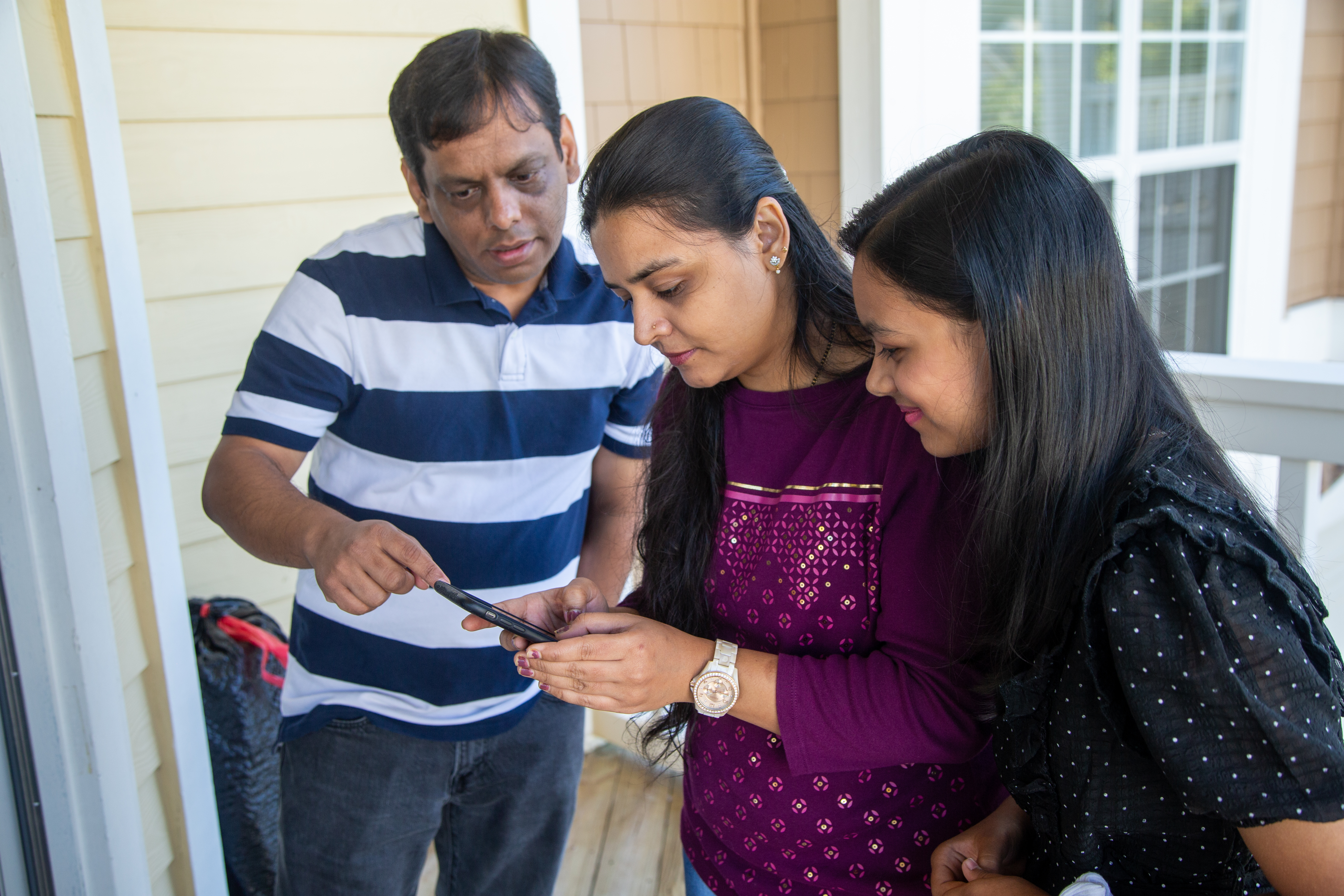 Mehul Bhatt (from left), his wife Hita and daughter Aesha work together on a phone in their home.
PHIL SKINNER FOR THE ATLANTA JOURNAL-CONSTITUTION.