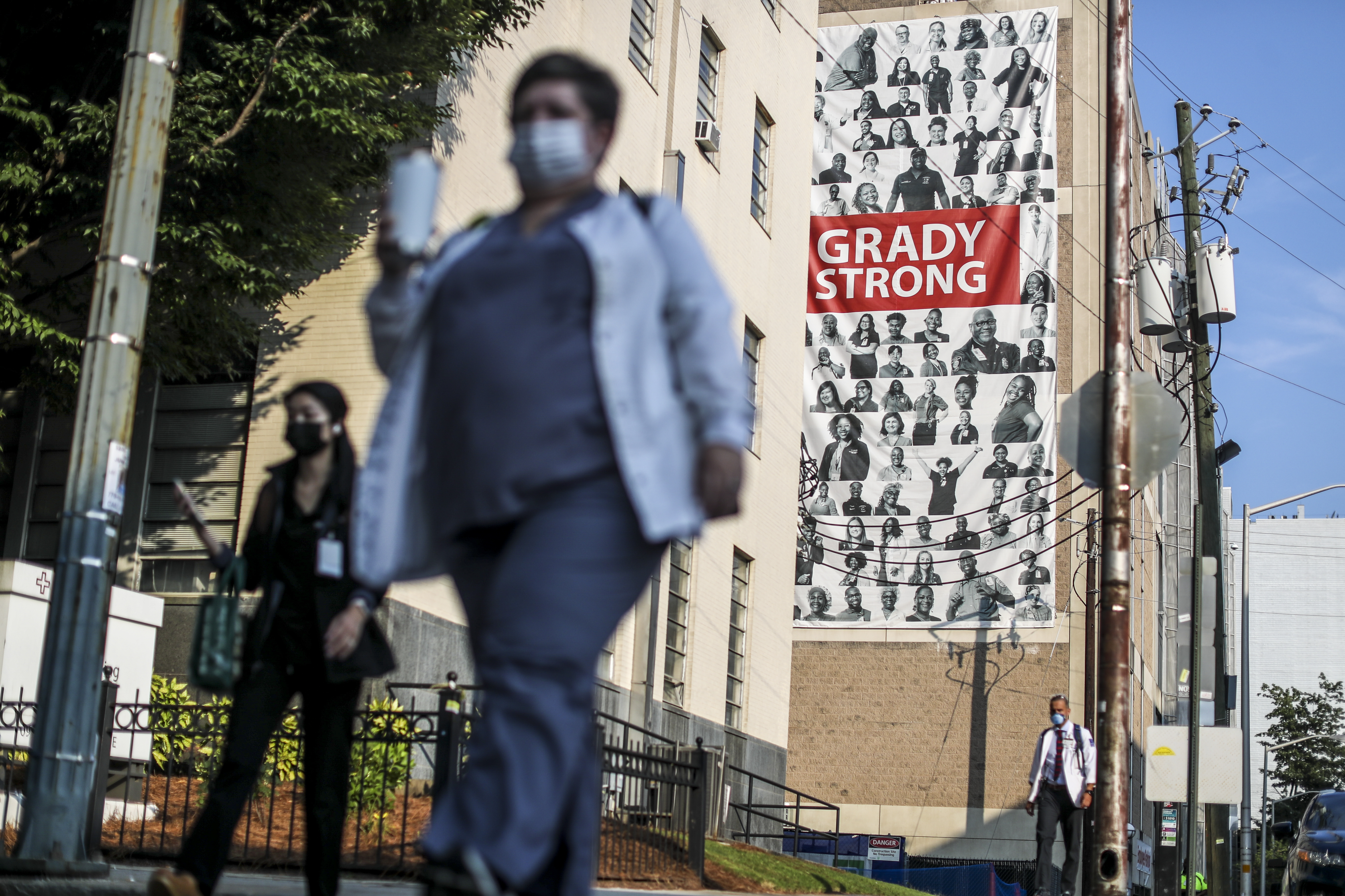 Medical workers arrive Tuesday, Aug. 10, at Grady Memorial Hospital against a large banner draped across the facade of a parking deck. COVID-19 cases are filling Georgia hospitals once again, igniting concerns of even more devastating outbreaks to come. (John Spink / John.Spink@ajc.com)