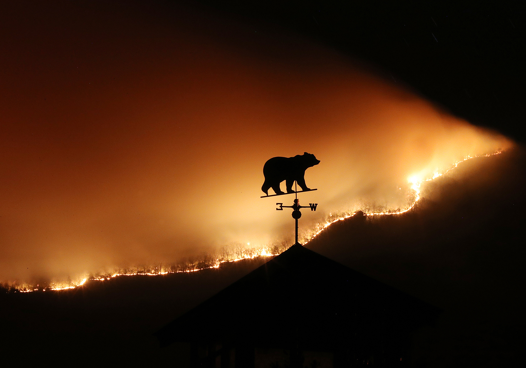 At first glance the weathervane on the top of a barn appears to be a bear fleeing the Rock Mountain Fire as it burns across the top of ridge pole above Bettyâs Creek Road where home owners are under a pre-evacuation order just north of Clayton. Thousands of acres have been burned by wildfires in the Georgia mountains from extreme drought conditions. Made with a Canon EOS 1DX Mark II camera, a 300 mm lens, 32 second, F/32, ISO 5000, and a tripod. Curtis Compton/ccompton@ajc.com