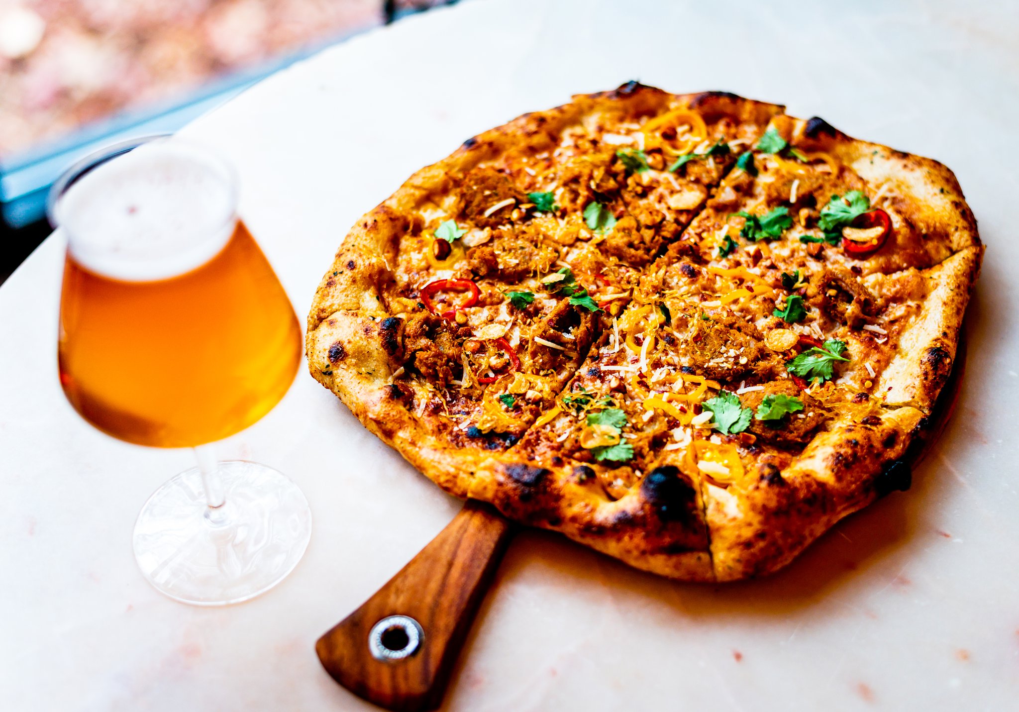 A pizza topped with Thai chile sausage, peanut sauce, pickled peppers and cilantro with a house-brewed beer. CONTRIBUTED BY HENRI HOLLIS