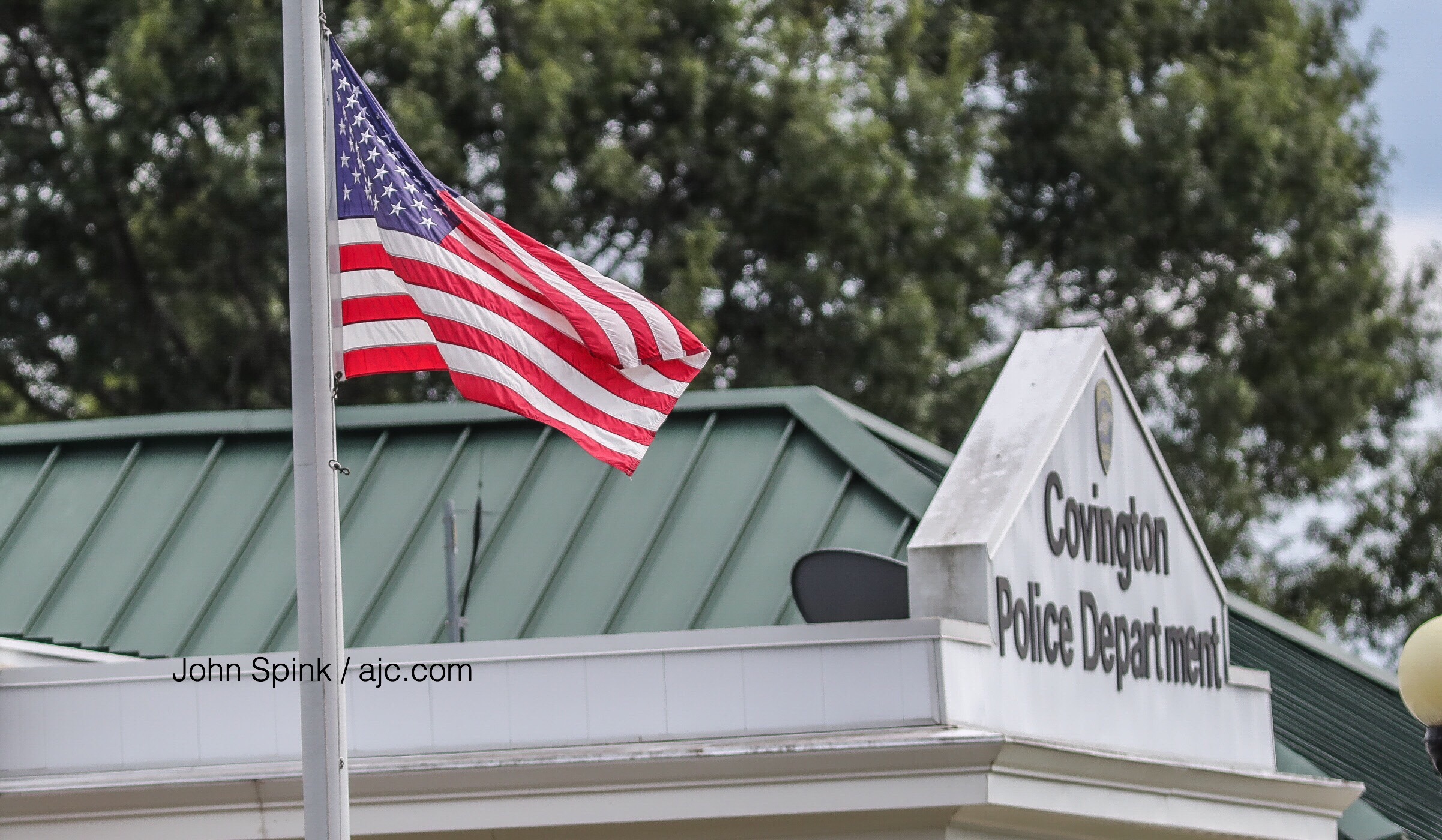 The American flag is flown at half-staff Monday at the Covington Police Department as Officer Matt Cooper is moved to Grady Memorial Hospital. JOHN SPINK / JSPINK@AJC.COM