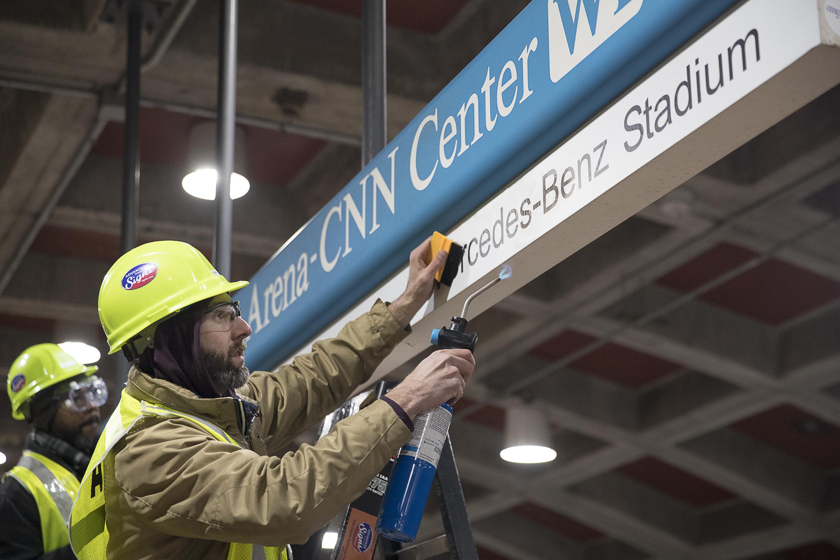 Tim Carl (second from left) of Advantage Graphics & Signs uses a torch to ensure the cohesiveness of the new Mercedes-Benz signage at the MARTA Dome/GWCC/Philips Arena/CNN Center Transit in Atlanta, Wednesday, Jan. 16, 2019. Advantage Graphics & Signs worked in the transit station on Wednesday to replace signage that mislabeled Atlanta's two newly named sport stadiums. (Alyssa Pointer/Alyssa.Pointer@ajc.com)