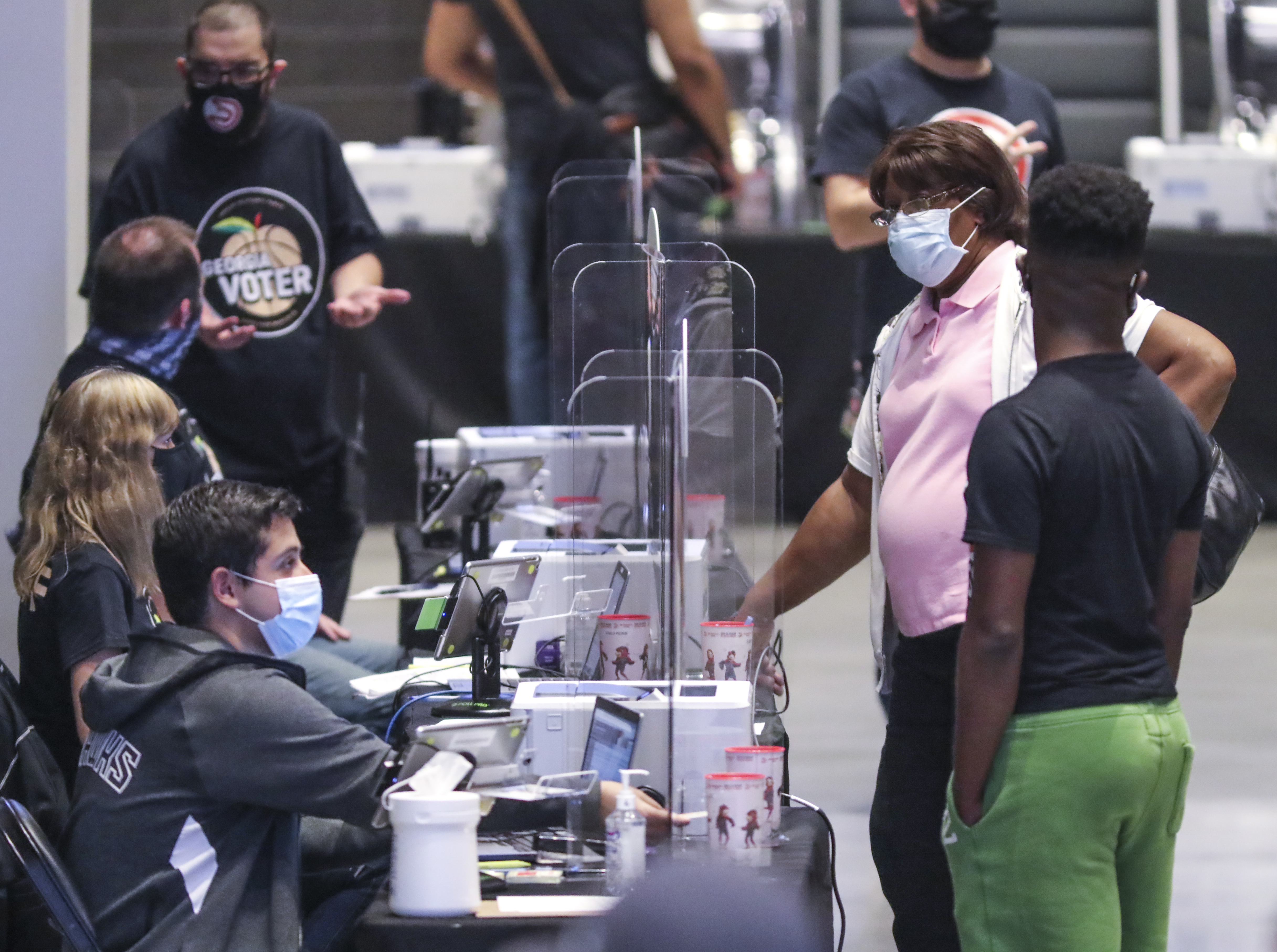 Poll workers check the identity and eligibility of people arriving for early voting on Oct. 12 at State Farm Arena in downtown Atlanta. An investigation by The Atlanta Journal-Constitution shows that Secretary of State Brad Raffensperger’s office weakened Georgia's voting system defenses, disabling password protections on a key component that controls who is allowed to vote. (John Spink / John.Spink@ajc.com)