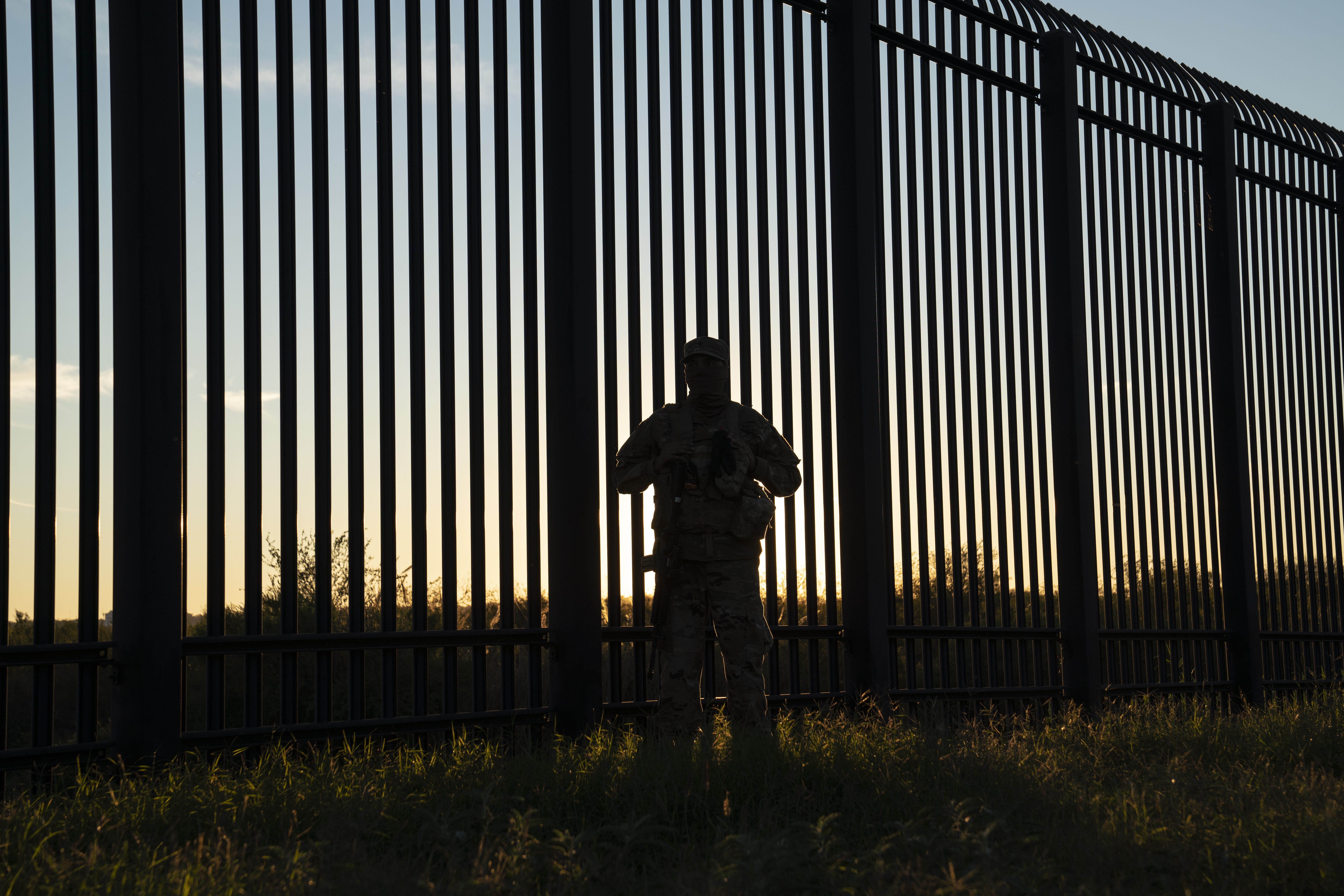 Three migrants who had managed to evade National Guard and cross the Rio  Grande onto U.S. territory wait for Border Patrol along a wall set back  from the geographical border, in El