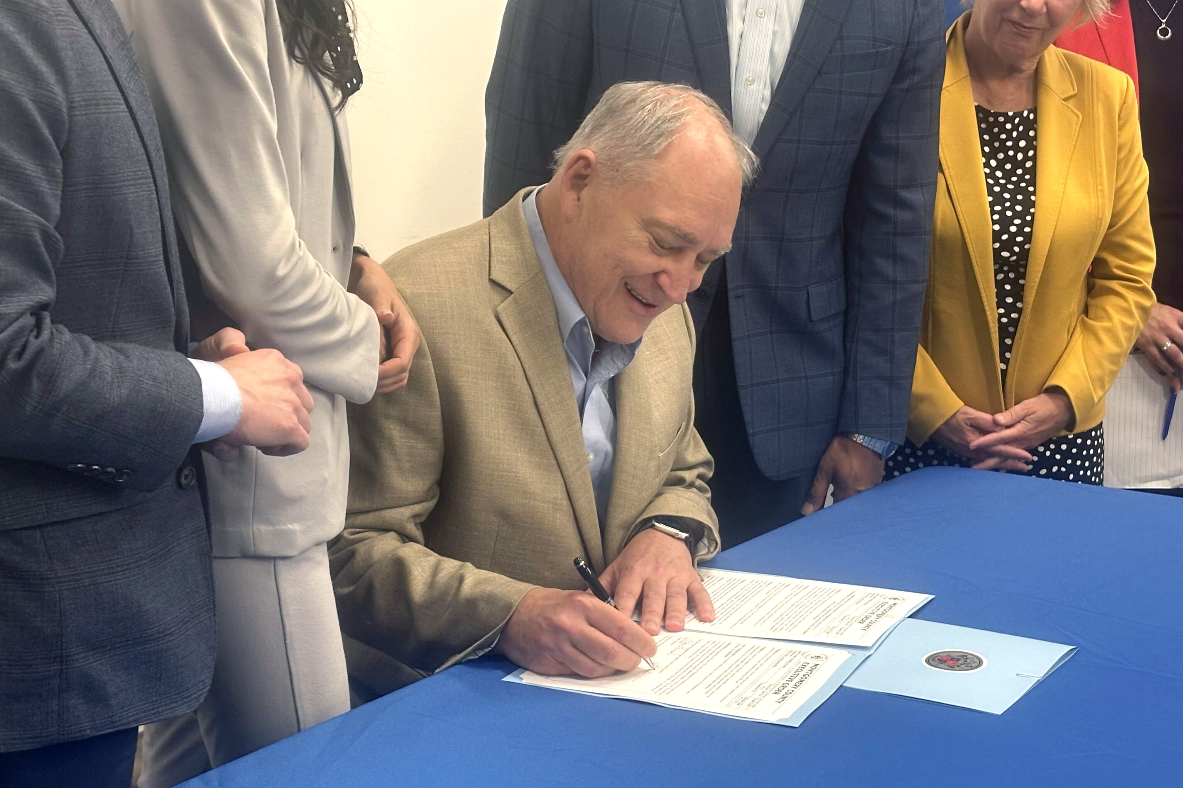 Montgomery County Executive Marc Elrich signs an executive order Friday issuing a six-month moratorium on data center permits, while flanked by supporters. The temporary ban is Elrich’s answer to months of debate on the issue.
