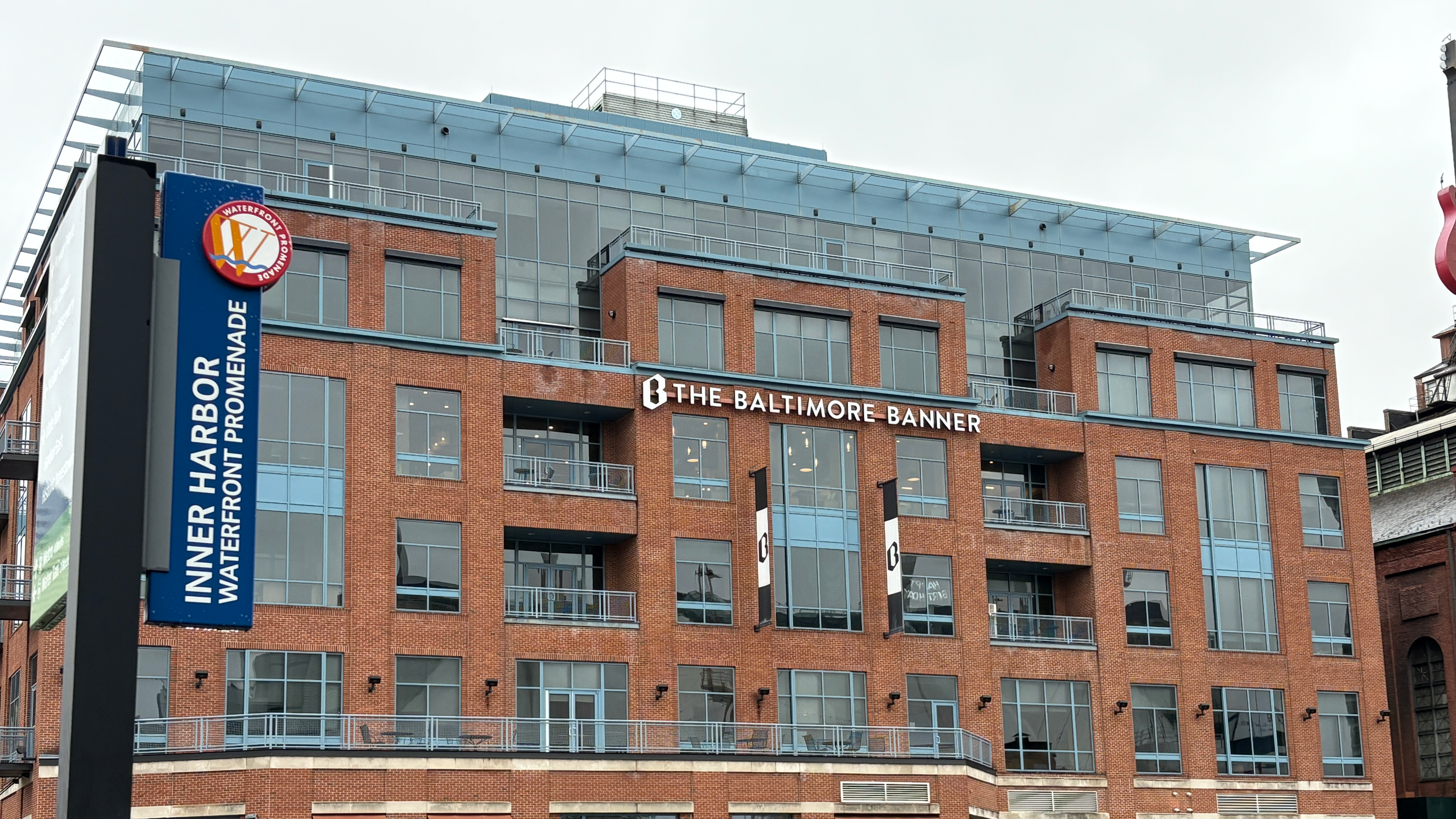 The exterior of the Baltimore Banner office building located in the city's Inner Harbor. A sign says Inner Harbor, Waterfront Promenade.