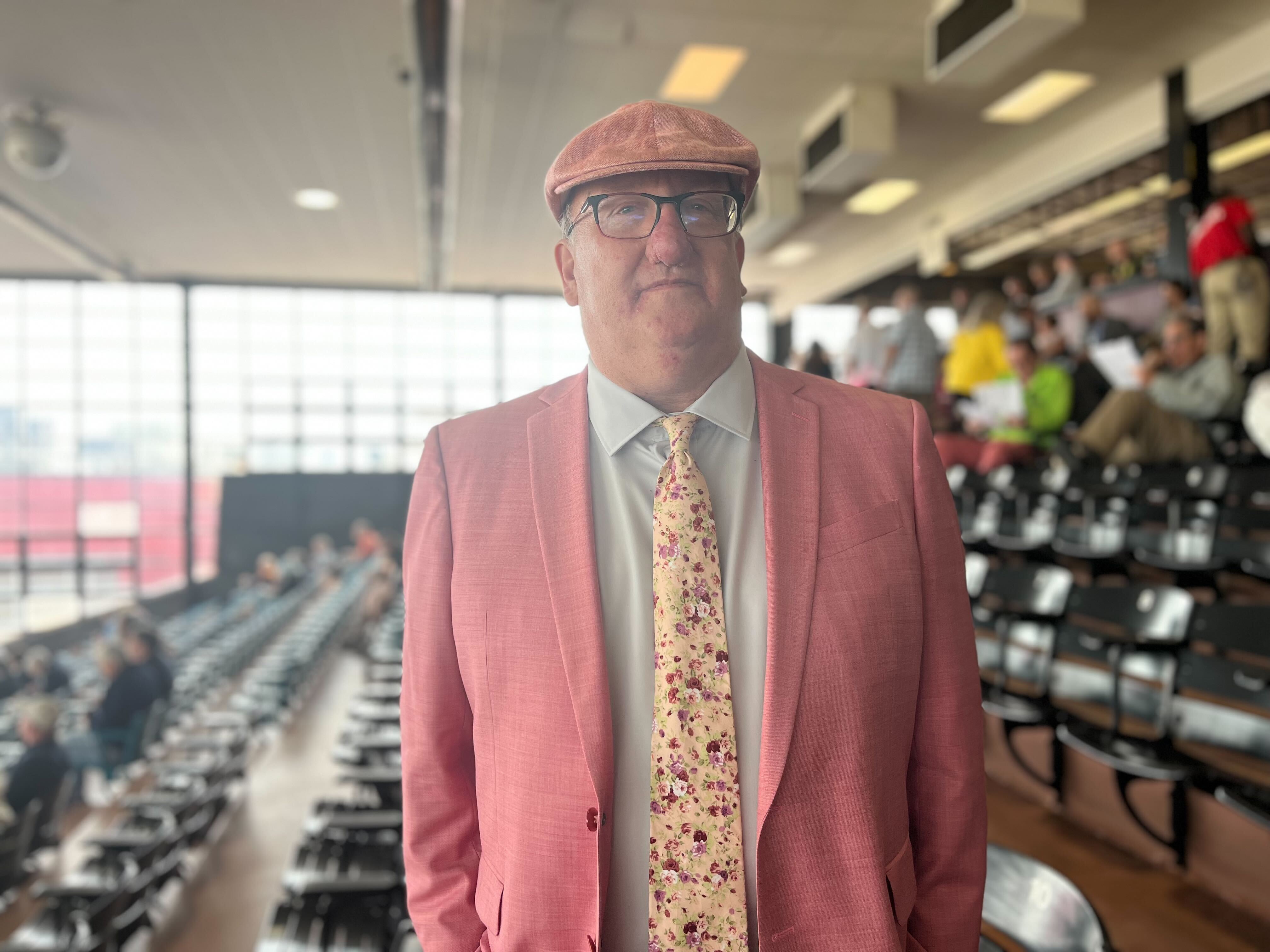 Steven Hettinger in a muted baby pink suit, matching cap and floral tie at Preakness. (Clara Longo de Freitas/The Baltimore Banner)
