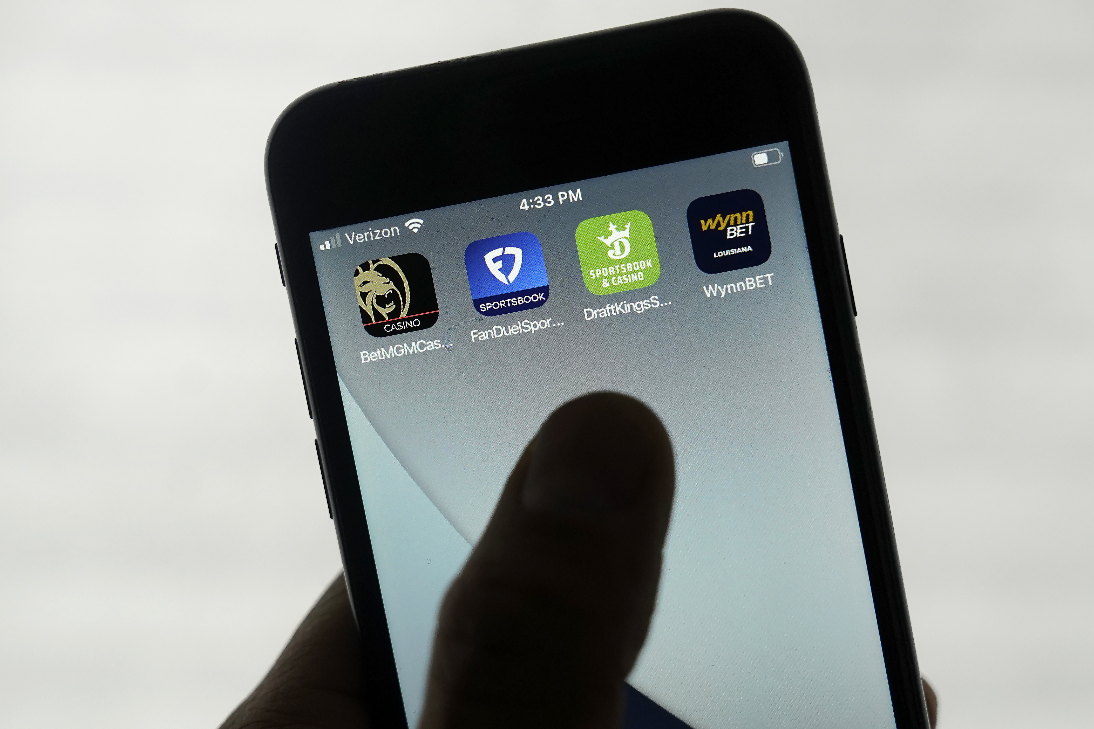 A hand hold a mobile phone with four sports betting apps displayed.