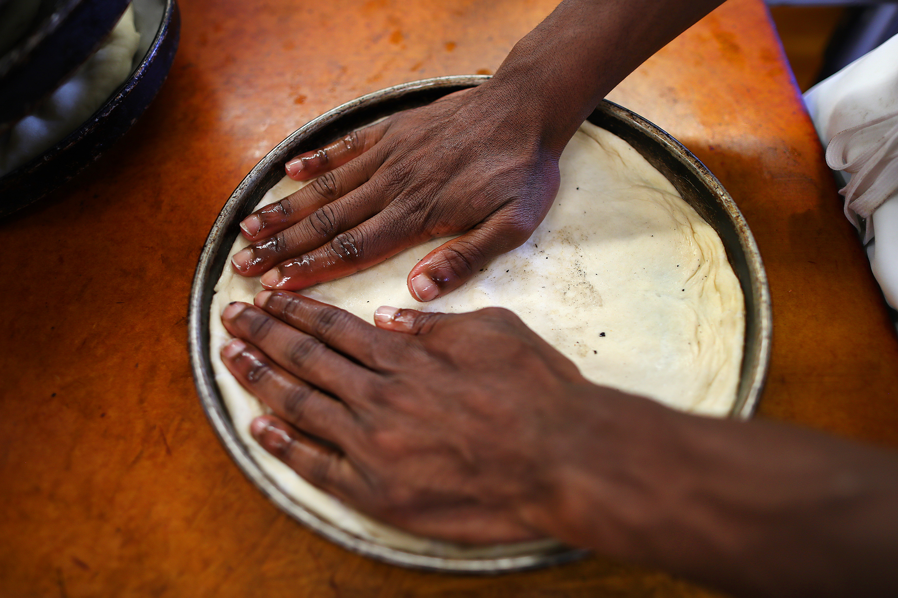 Cook Audley Jean-Baptiste forms the dough in the pan and makes small dimples with his fingertips to catch the flavors from the melted cheese.