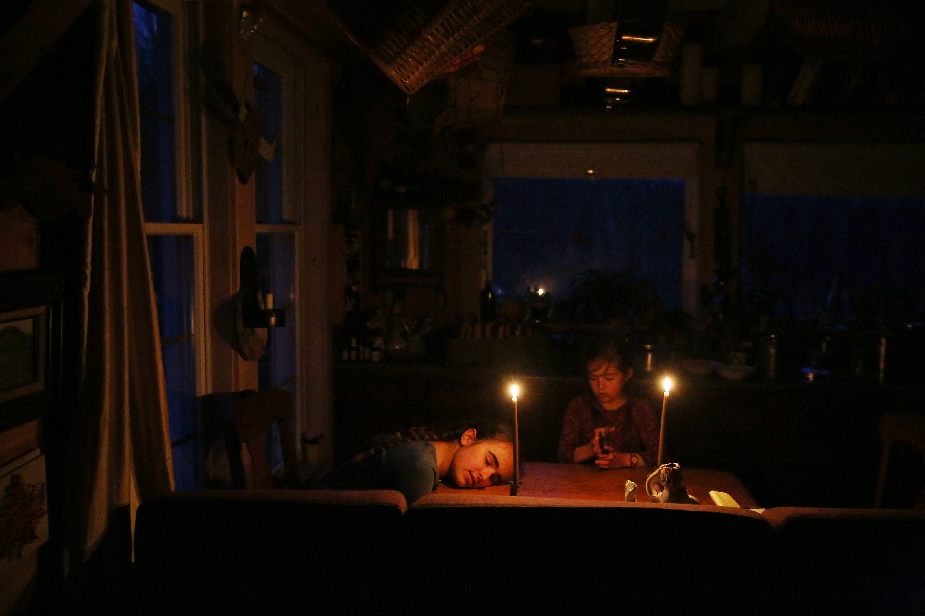 After a long day, Etta Hughes rested her head on the table while she and her sister Isla played cards. Etta and Isla live with their parents on an off-the-grid permaculture homestead in Belfast, Maine.