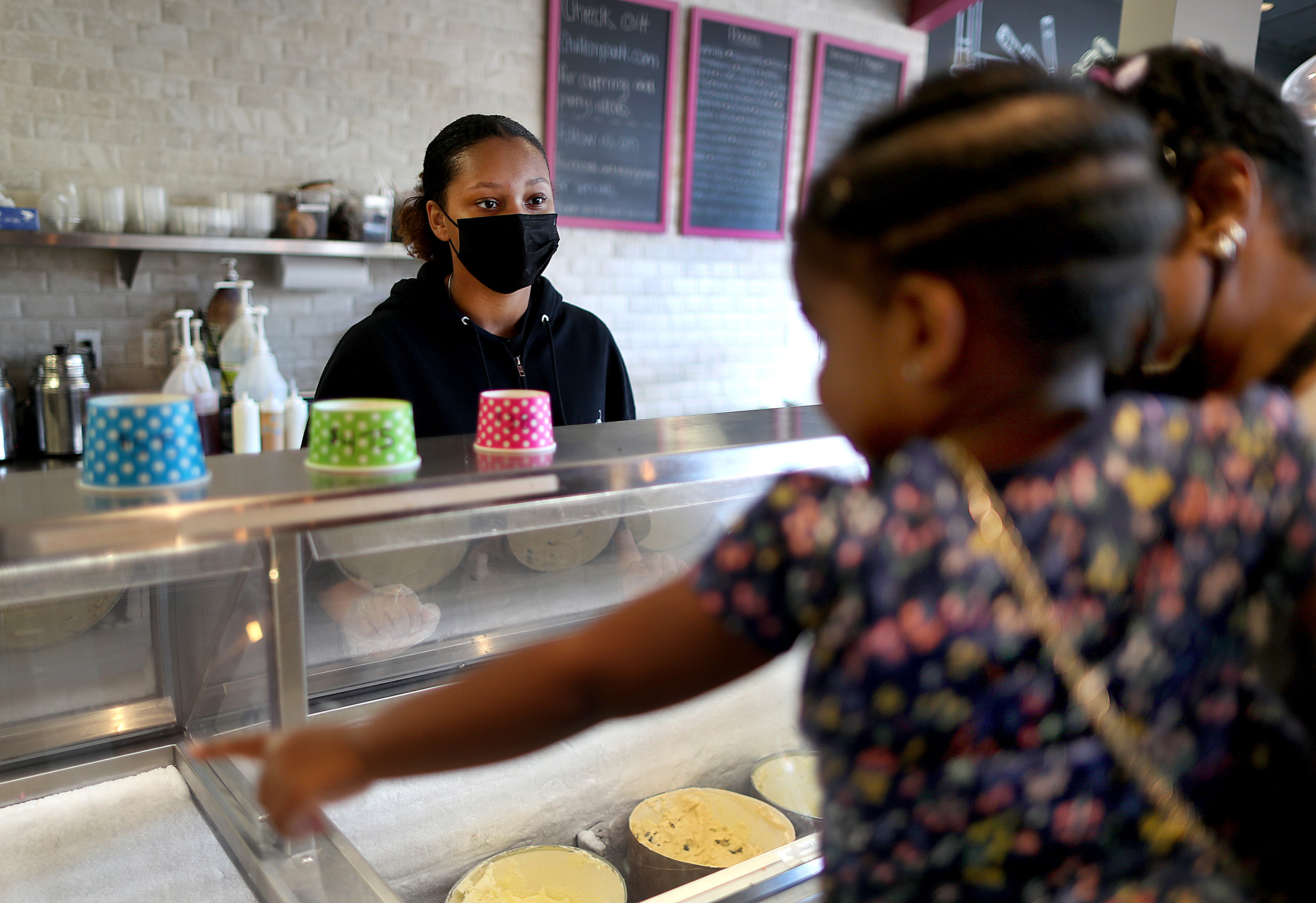Teenage worker at Chill on Park, Unique Berry, waits on Nova Harrison, 2, held by her mother Angie Pullum, as she points out the flavor she wants.