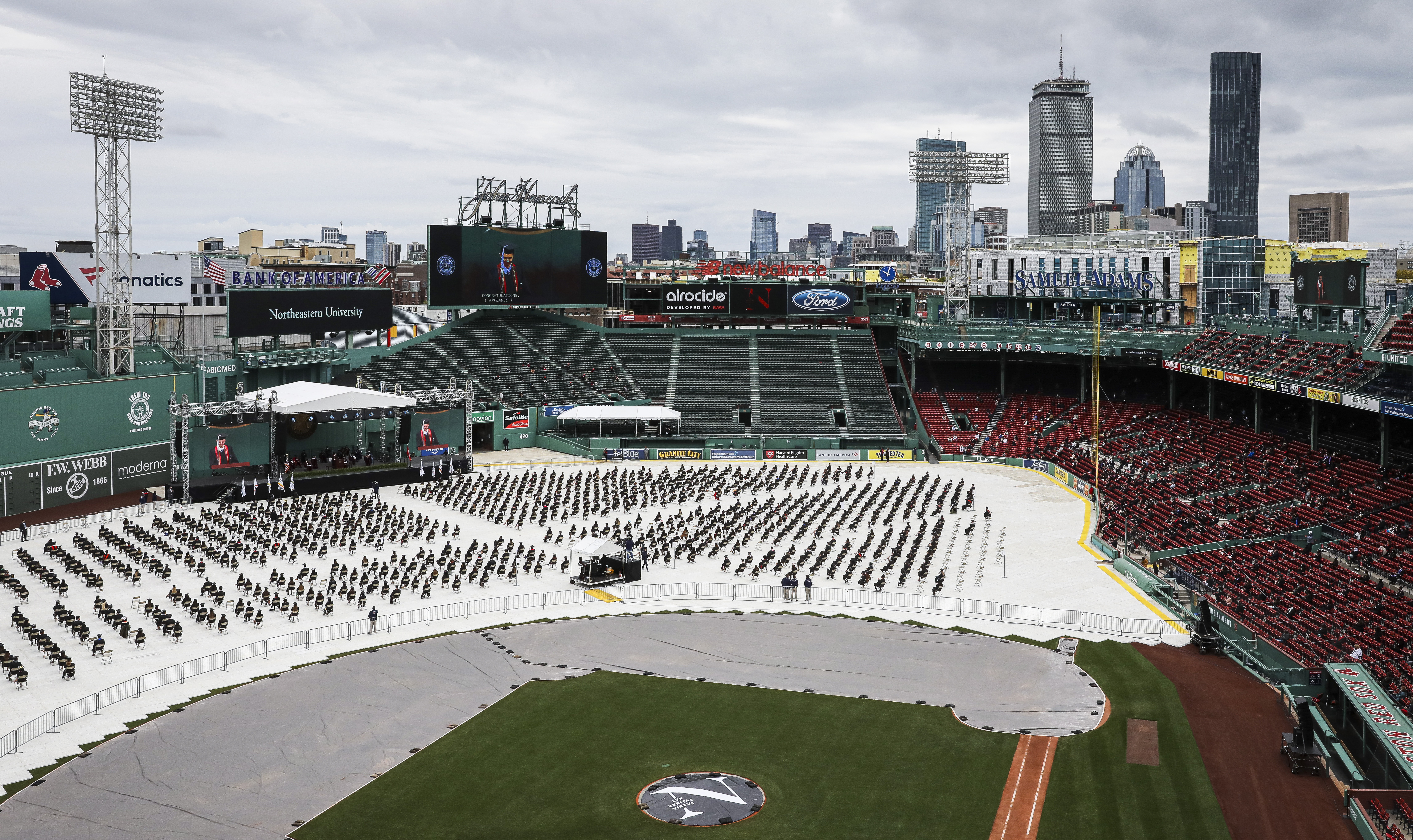 MAY 8, BOSTON  —  This is the Northeastern University class of 2021 commencement at Fenway Park. I shot this from the Green Monster Deck. Some students were sitting in the stands and some were out on the baseball field all spaced out, with this white cloth covering it. It made for this incredibly cool pictorial in their black gowns wearing their little black caps. I think they were only allowed to bring one person with them, because I remember thinking how sad that would have been, to have to pick one parent or the other to attend the ceremony. – Erin Clark